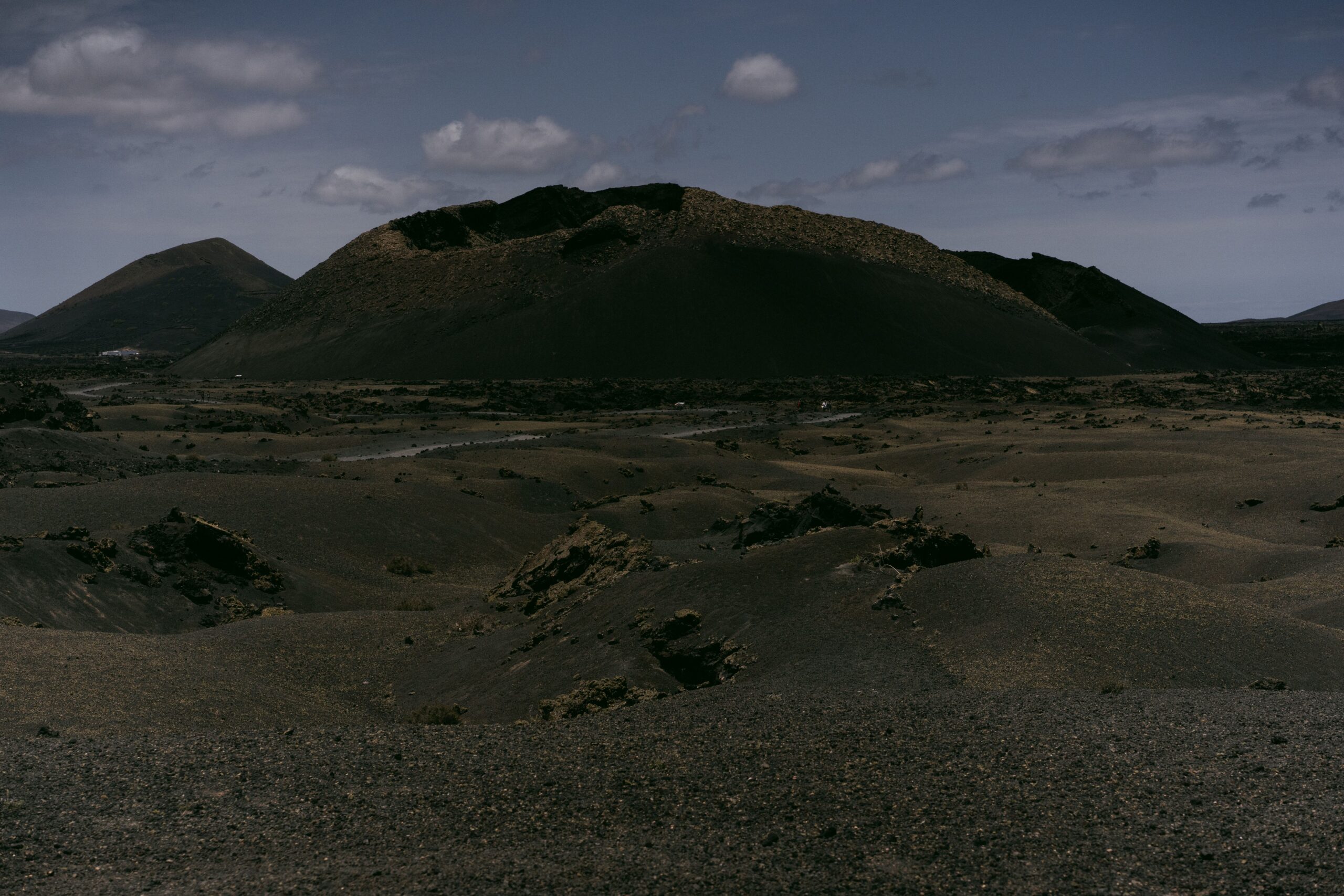 Yermo volcánico desolado con suelo de obsidiana oscura y formaciones rocosas irregulares bajo un cielo melancólico, evocando un entorno devastado por la guerra.