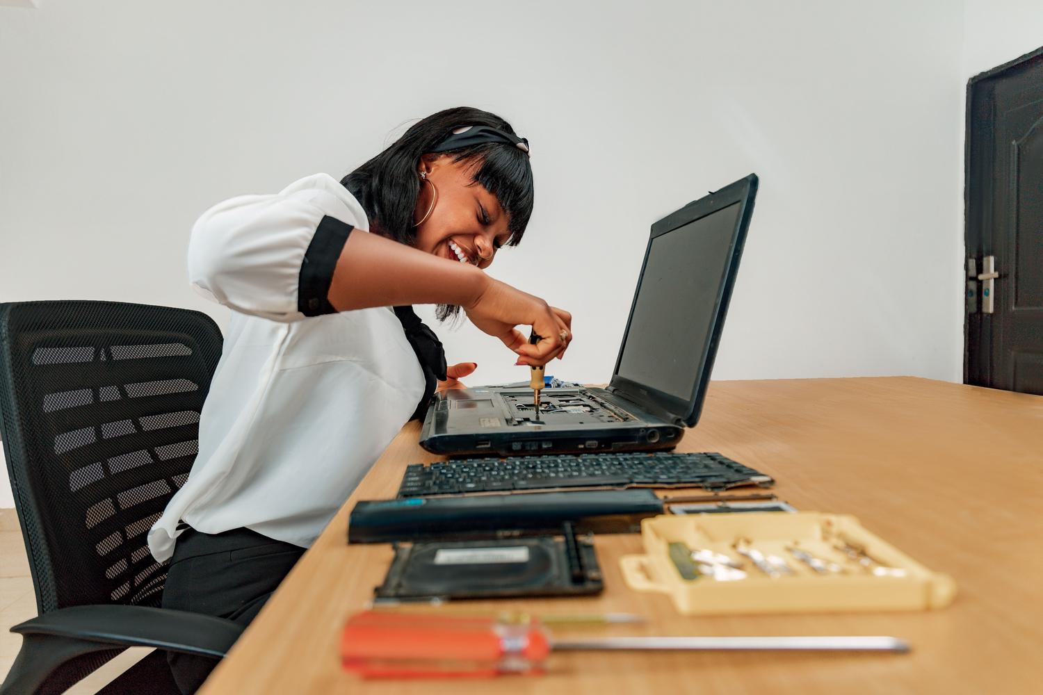 Mujer técnica reparando un ordenador portátil en un escritorio con herramientas, representando el mantenimiento de hardware.