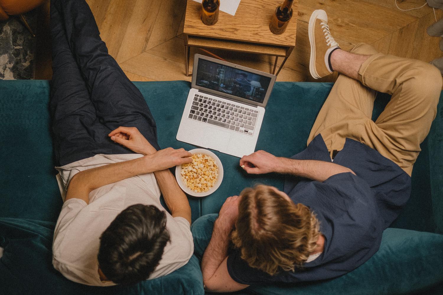 Dos amigos disfrutando de una sesión de streaming de anime con palomitas en un sofá acogedor