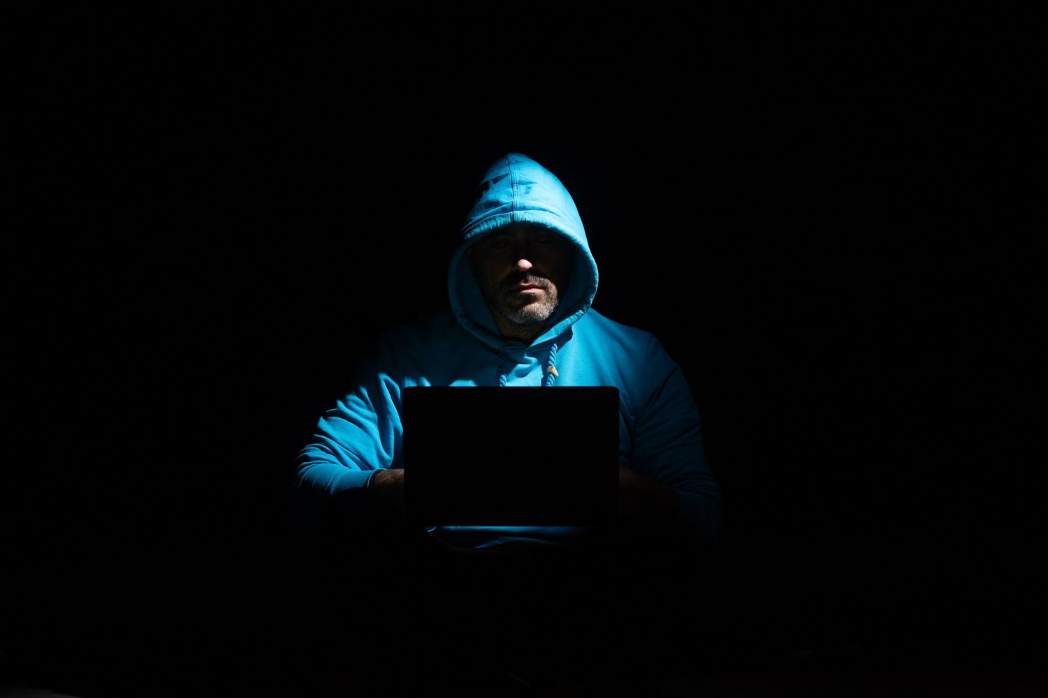 Persona anónima con capucha utilizando un portátil en una habitación oscura, representando el misterio de los autores de creepypastas.