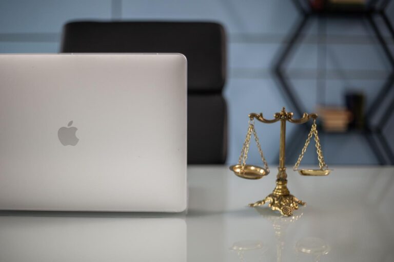 Equilibrio entre la tecnología y la ley: un ordenador portátil y una balanza de la justicia sobre un escritorio blanco.