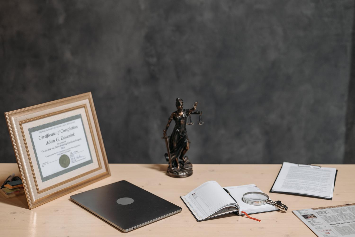 Escritorio de abogado con estatua de la justicia, documentos y una lupa, simbolizando el análisis de la propiedad intelectual.
