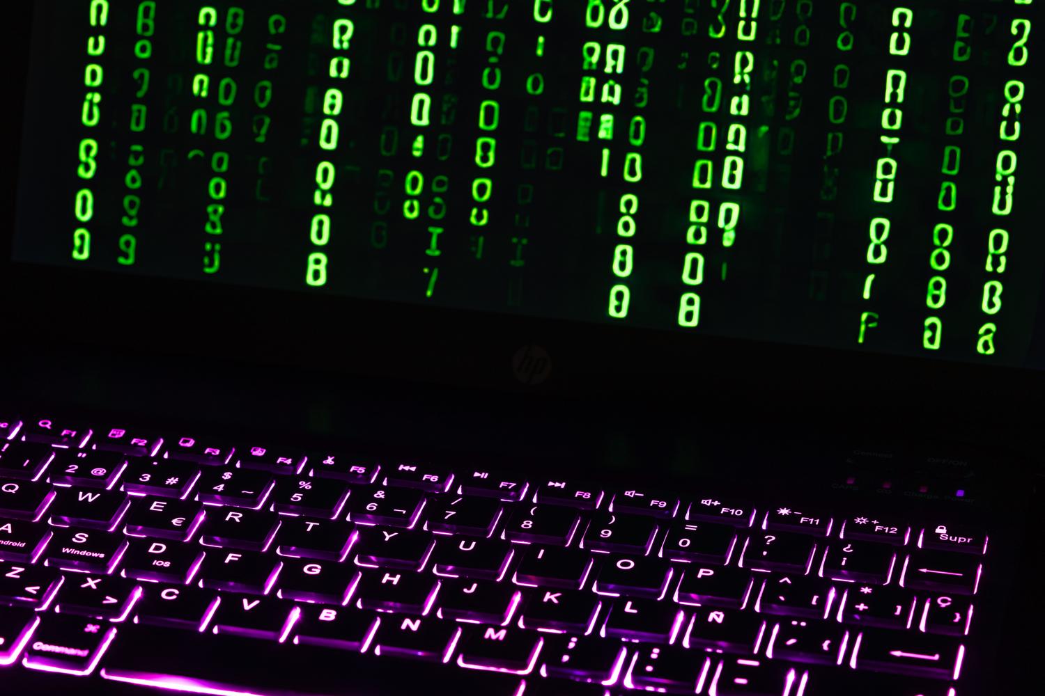 Teclado de portátil iluminado con código digital estilo Matrix en la pantalla, evocando la escritura de código blindado y seguro.