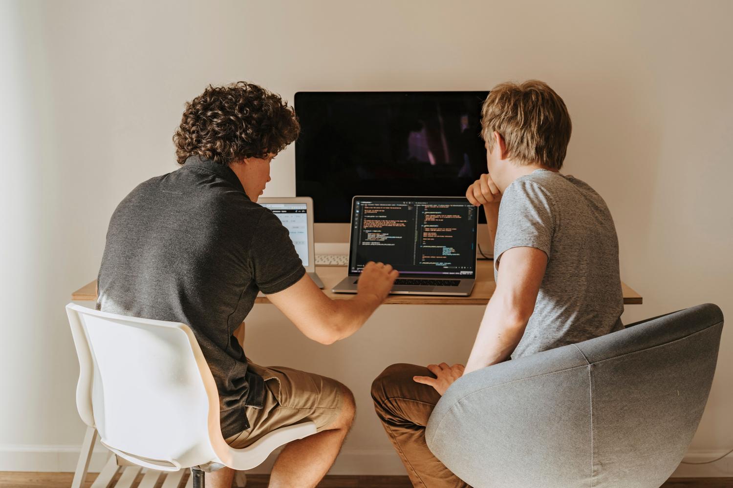 Dos desarrolladores de software colaborando y revisando código en un portátil, simbolizando la cultura de responsabilidad compartida en DevSecOps.