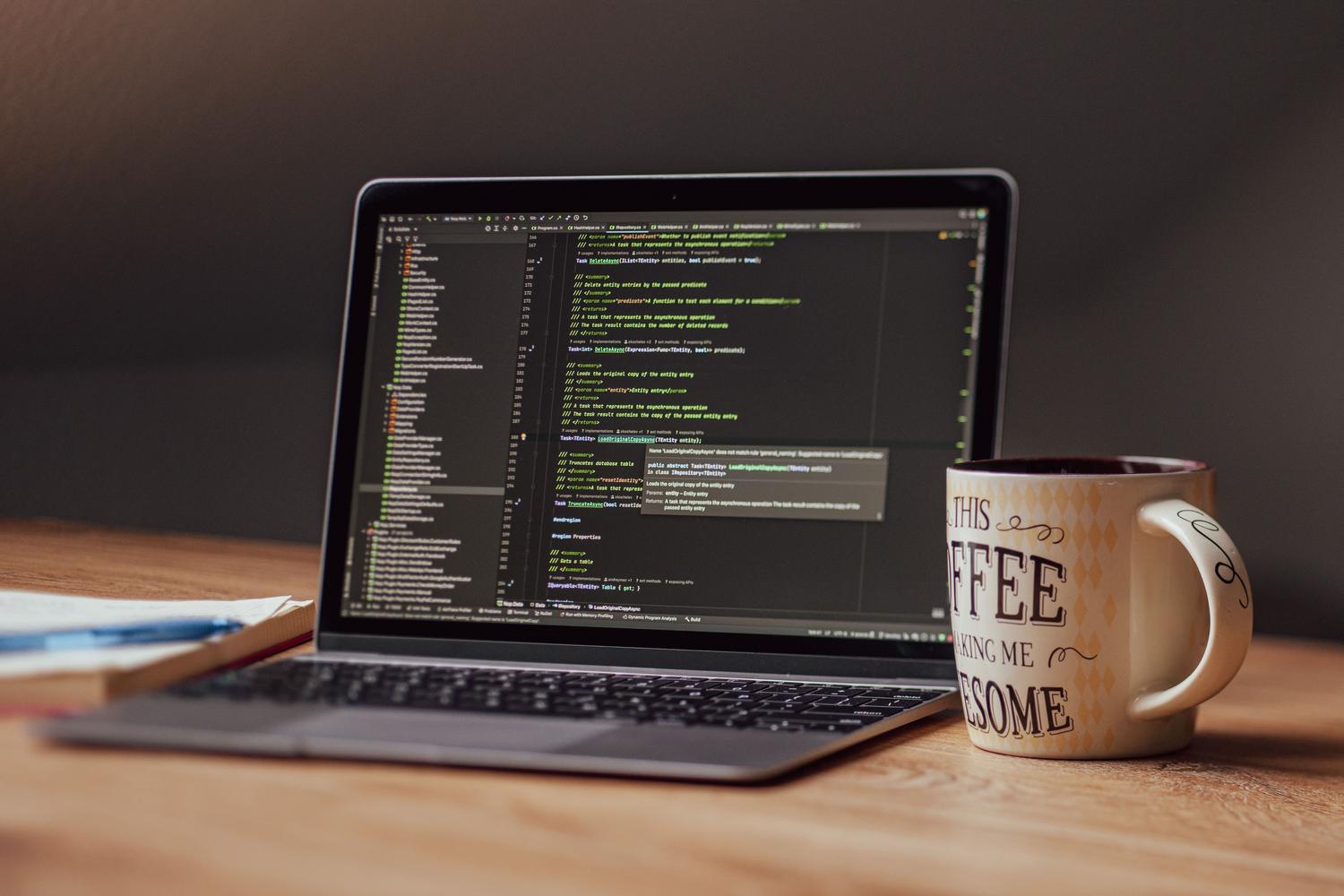 Espacio de trabajo moderno con un portátil mostrando un editor de código y una taza de café, integrando el uso de software en la vida cotidiana.