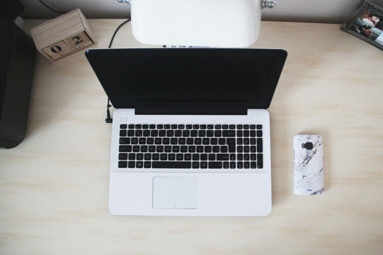 Vista cenital de un espacio de trabajo minimalista con un ordenador portátil, smartphone y accesorios de oficina.