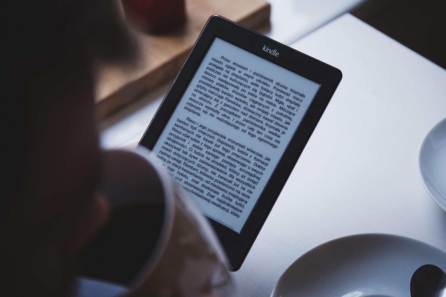 Persona leyendo en un lector de libros electrónicos junto a una taza de café, ilustrando el placer de una biblioteca digital bien organizada.