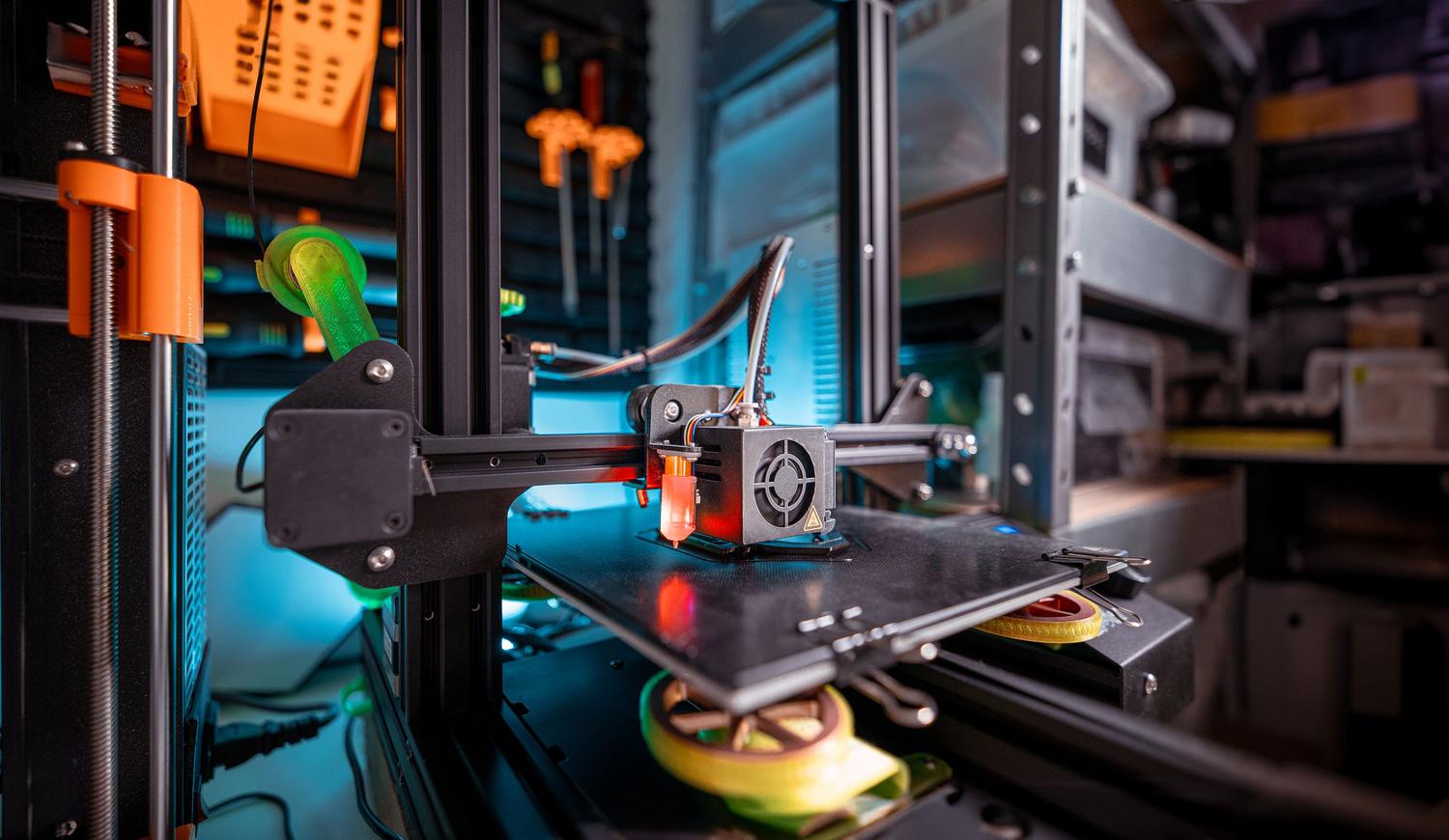 Taller de prototipado técnico con una impresora 3D en funcionamiento, rodeado de herramientas y equipo de ingeniería.