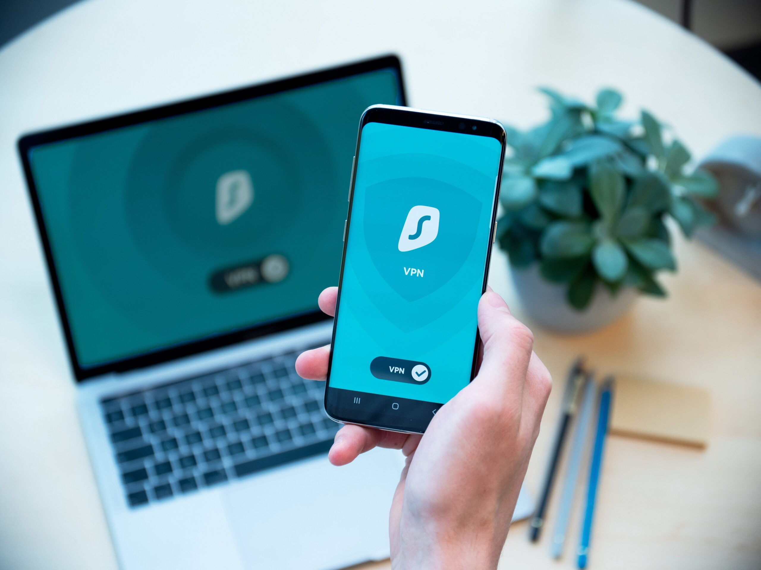 Smartphone y ordenador portátil sincronizados con una aplicación de VPN activa, mostrando la seguridad digital en múltiples dispositivos.