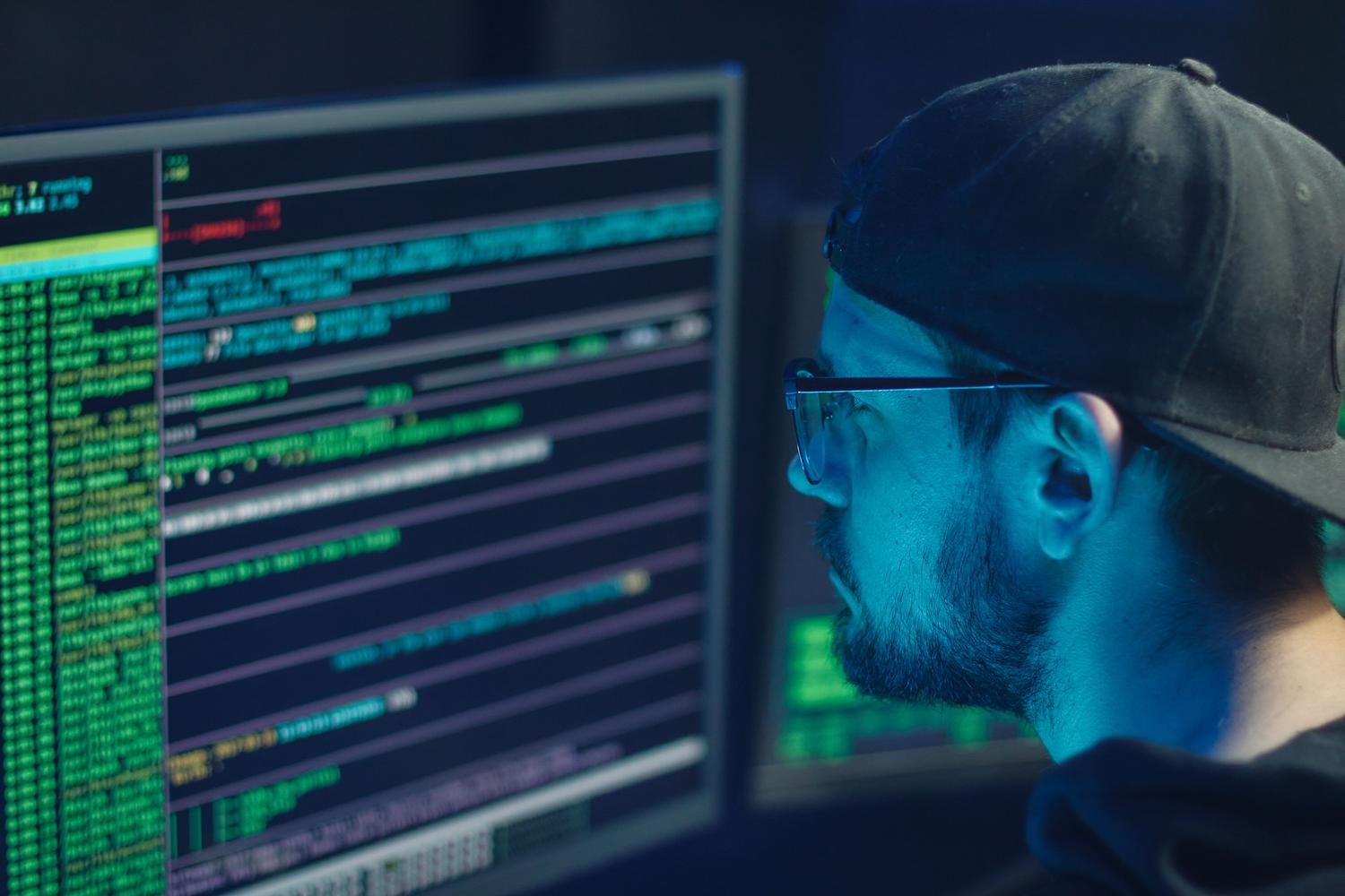 Profesional de ciberseguridad analizando líneas de código y logs en monitores en un entorno oscuro, representando al equipo de TI o SOC.