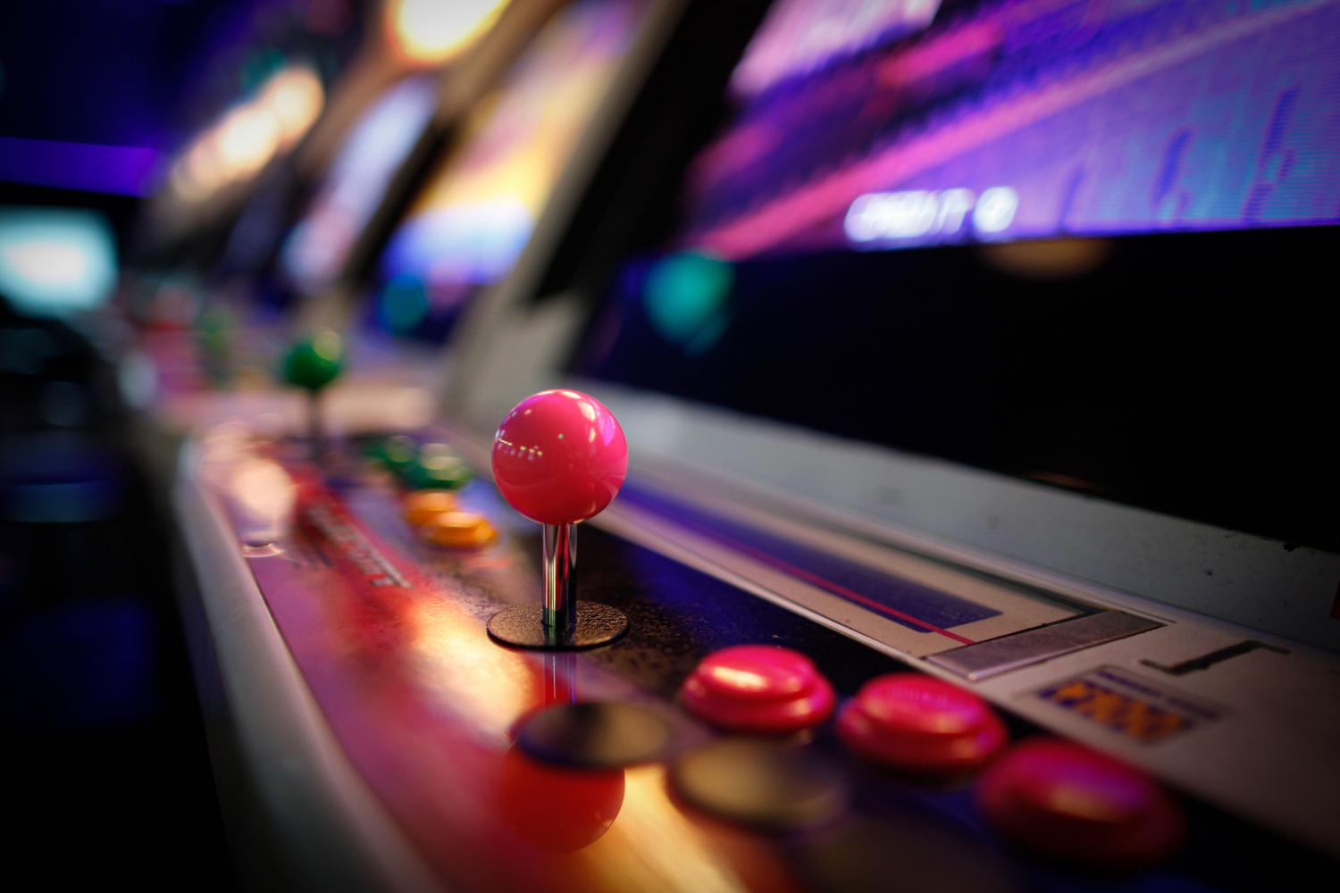 Detalle de una máquina recreativa vintage con joysticks y botones iluminados en un salón arcade, evocando la cultura de los salones recreativos.