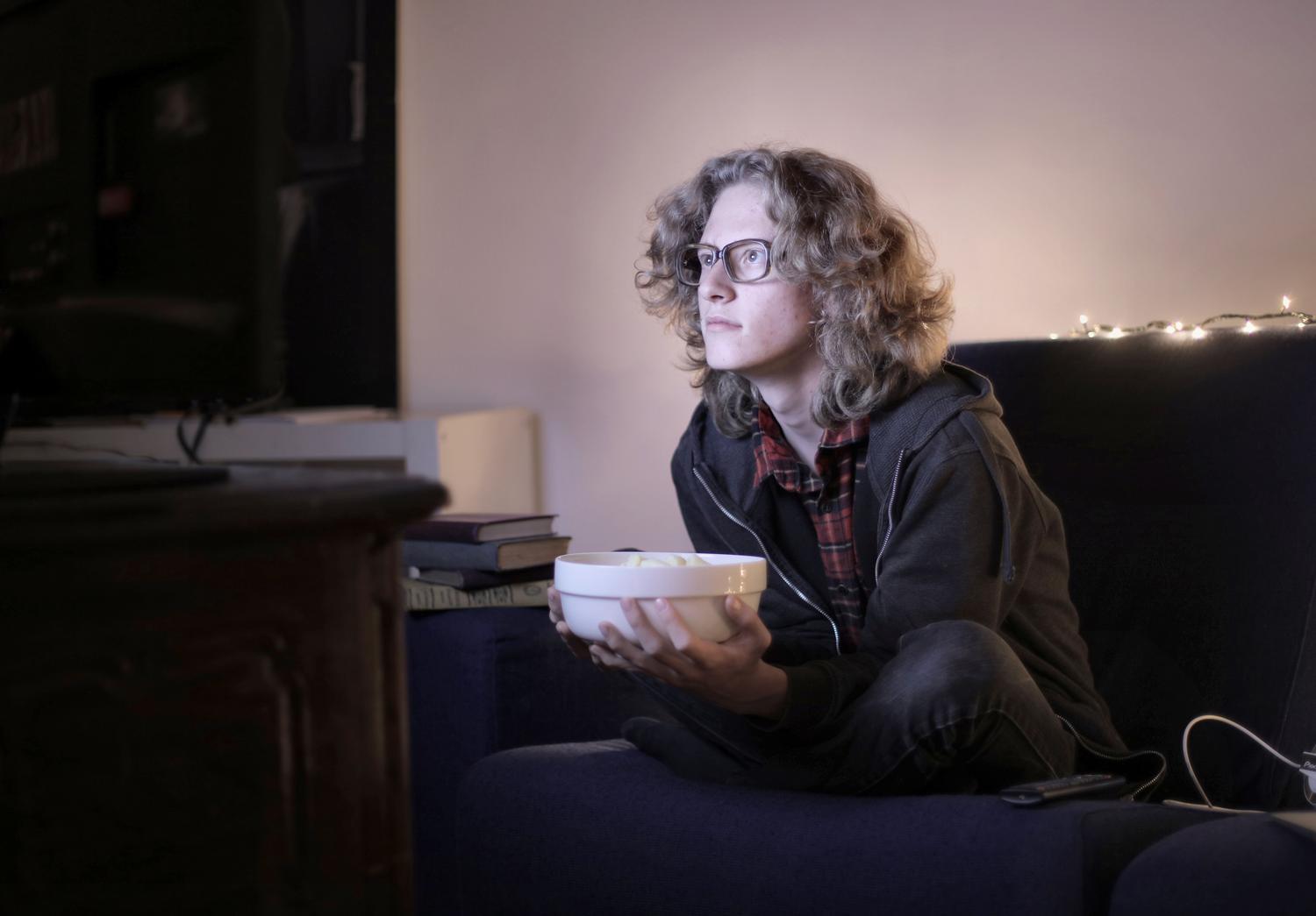 Un adolescente concentrado viendo una serie con un bol de palomitas.