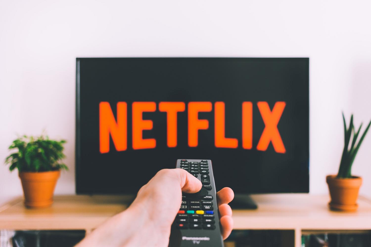 Primer plano de una mano sosteniendo el mando a distancia frente a una pantalla de streaming.