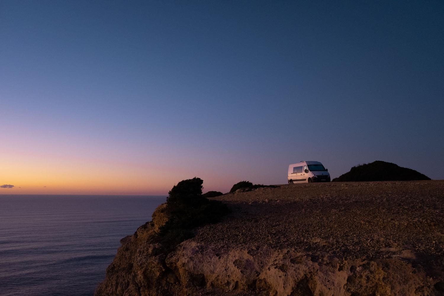Autocaravana aparcada en un acantilado frente al mar al atardecer, simbolizando la libertad de los nómadas digitales.