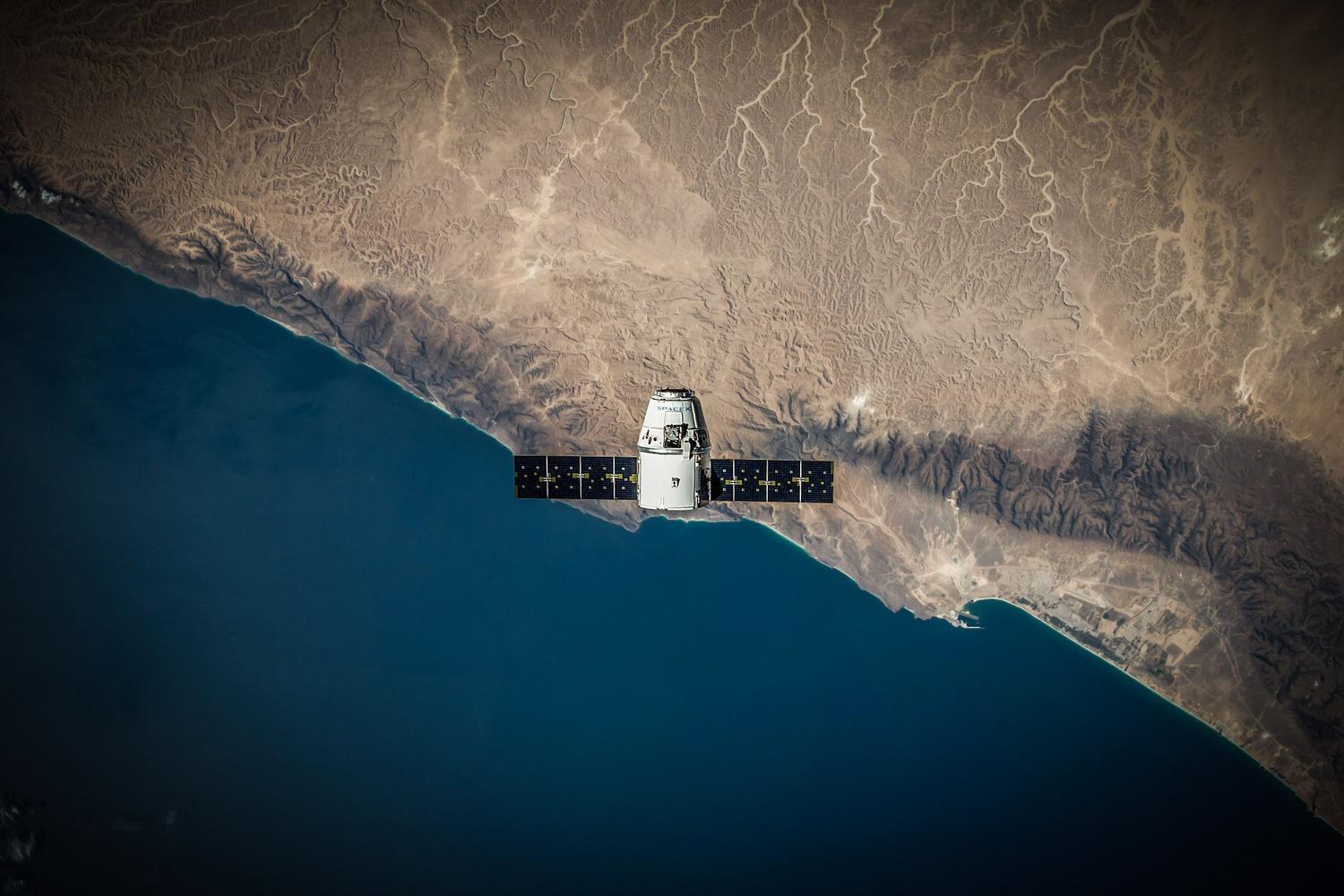 Satélite artificial orbitando la Tierra sobre la costa, representando la tecnología de constelaciones LEO de Starlink.