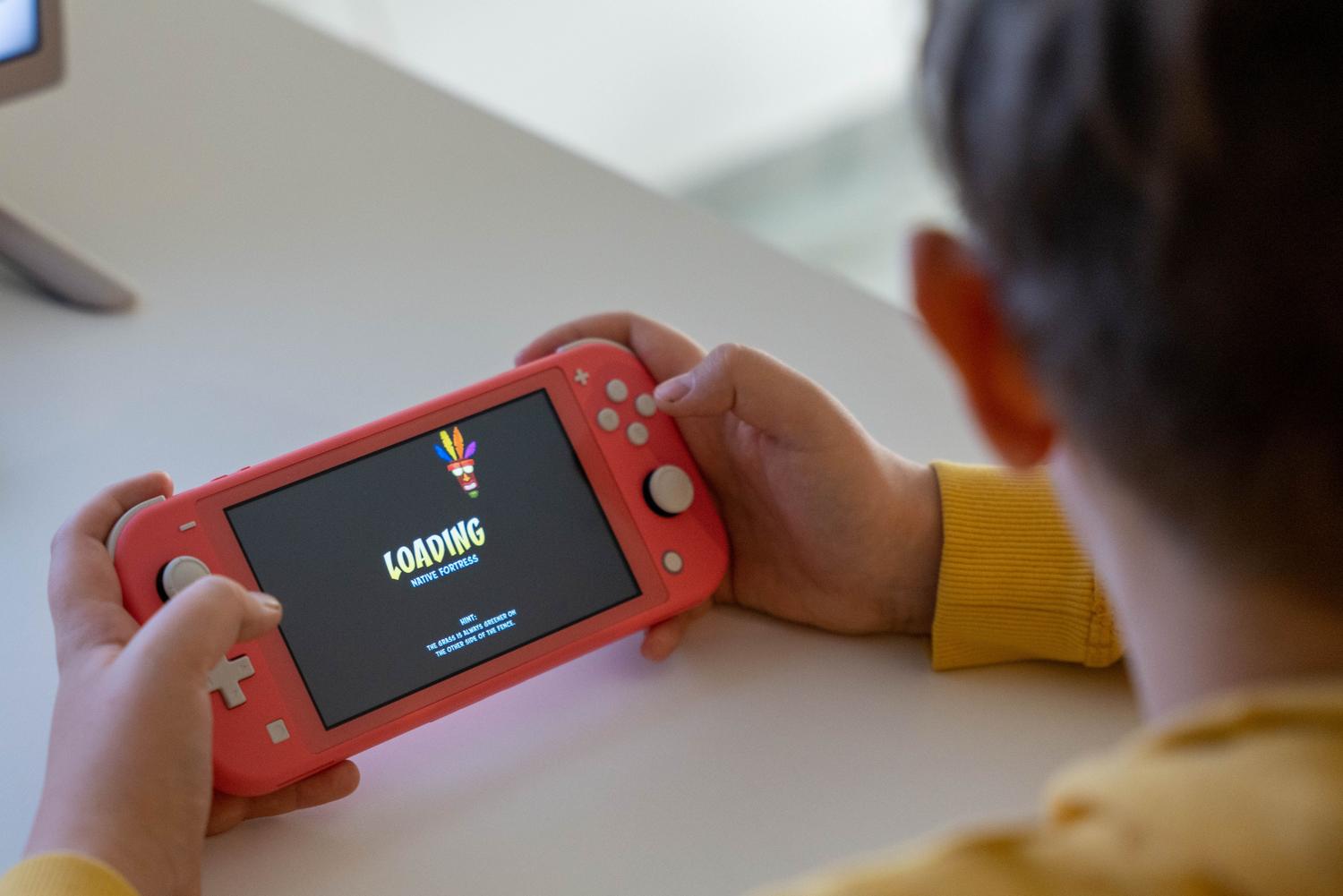 Niña sosteniendo una Nintendo Switch Lite de color coral mientras carga un juego en la pantalla.