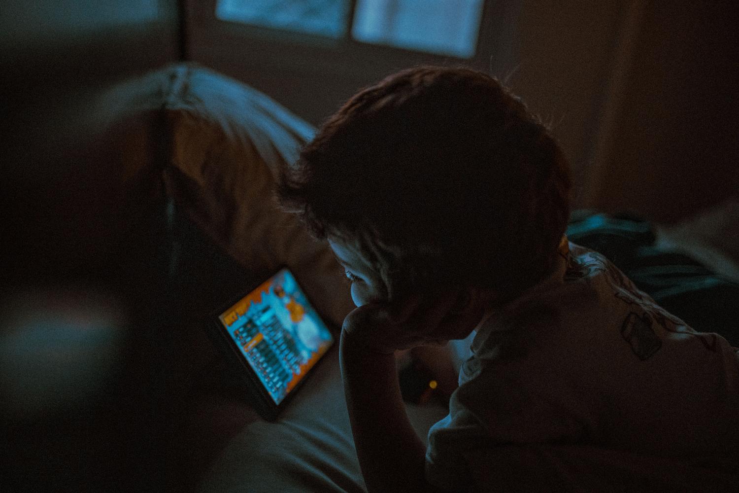 Niño jugando con un dispositivo electrónico en una habitación a oscuras, ilustrando la importancia de los límites horarios nocturnos.