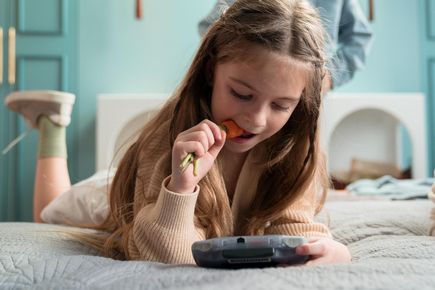 Niña jugando con una consola portátil en la cama, representando el ocio digital en el dormitorio.