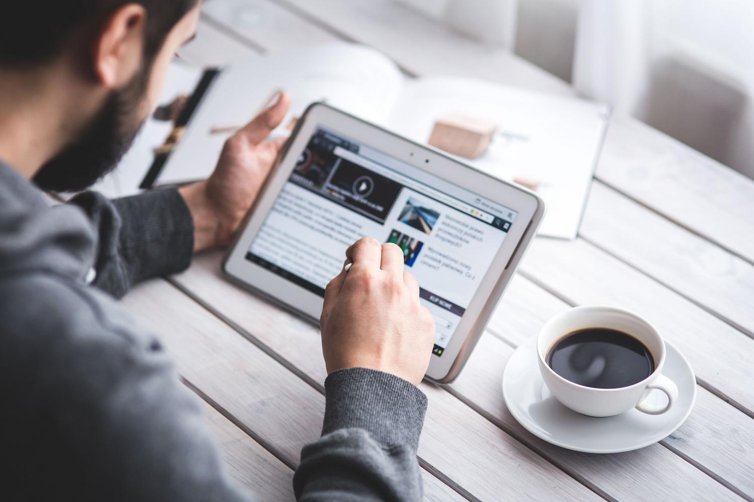 Hombre leyendo noticias y feeds en una tablet mientras toma un café, ilustrando el consumo moderno de contenidos RSS.