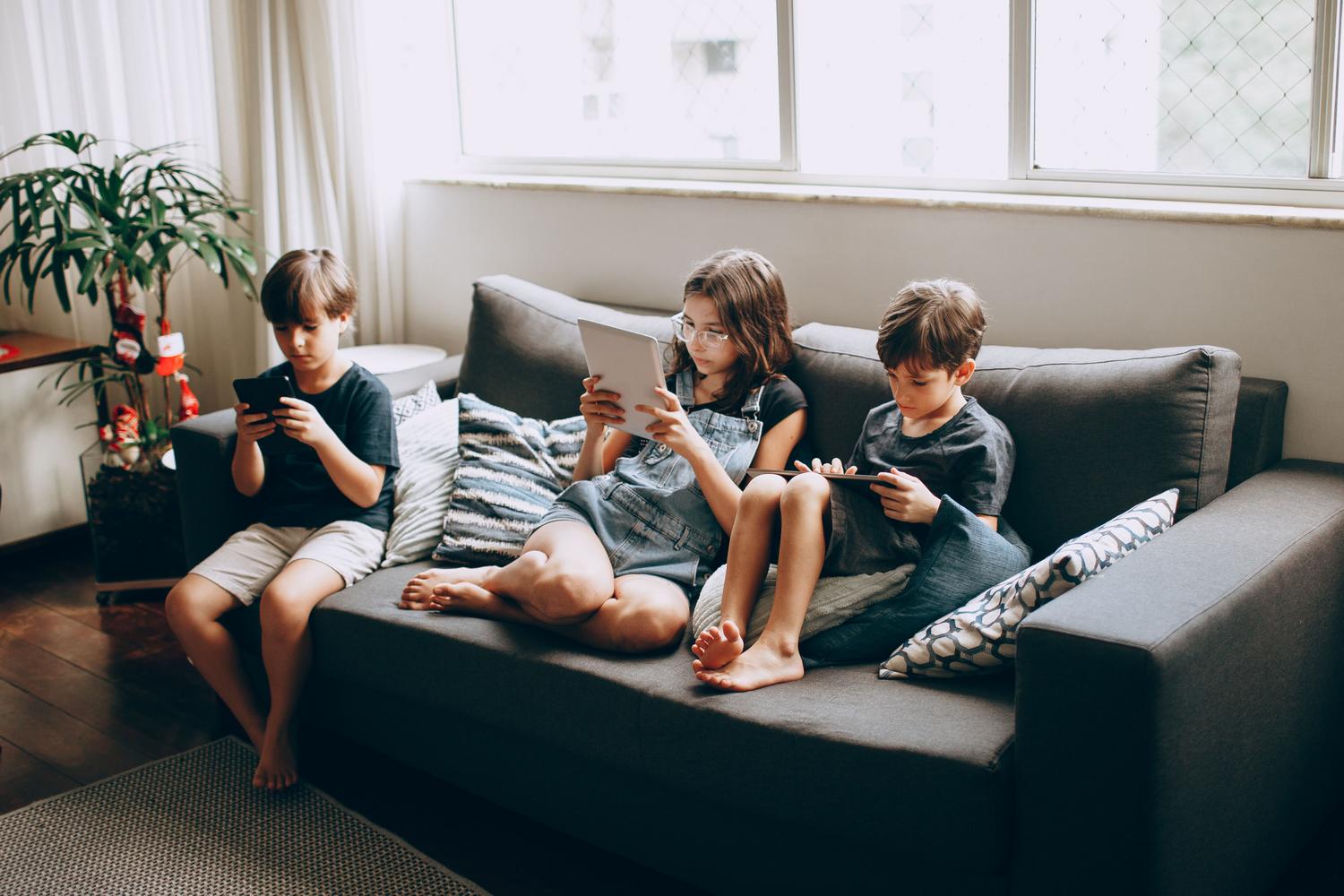 Niños utilizando dispositivos digitales en el sofá de una casa, ilustrando la vulnerabilidad de los usuarios en el hogar.