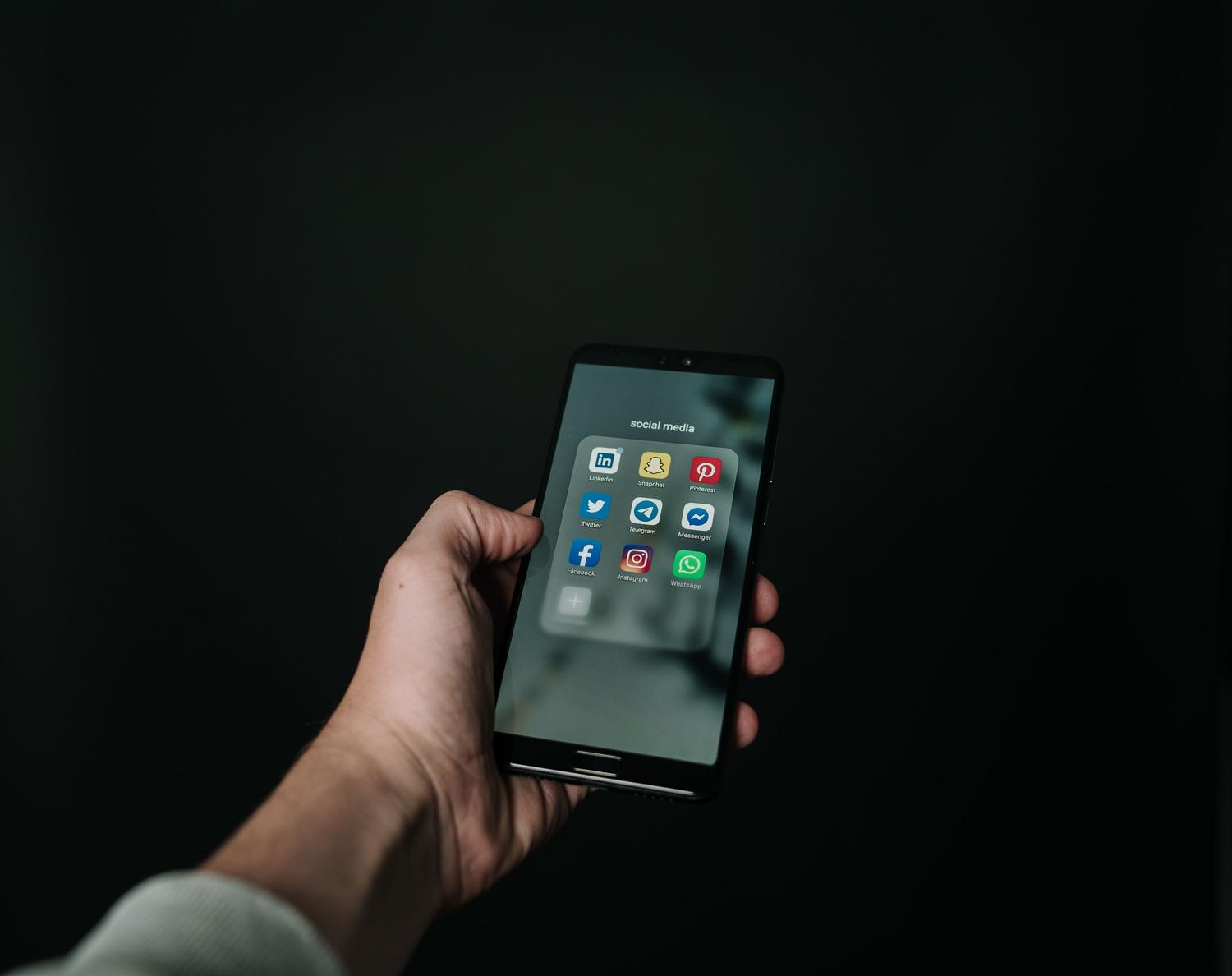 Primer plano de una mano sosteniendo un smartphone con una carpeta de aplicaciones de redes sociales, representando la centralización de enlaces.