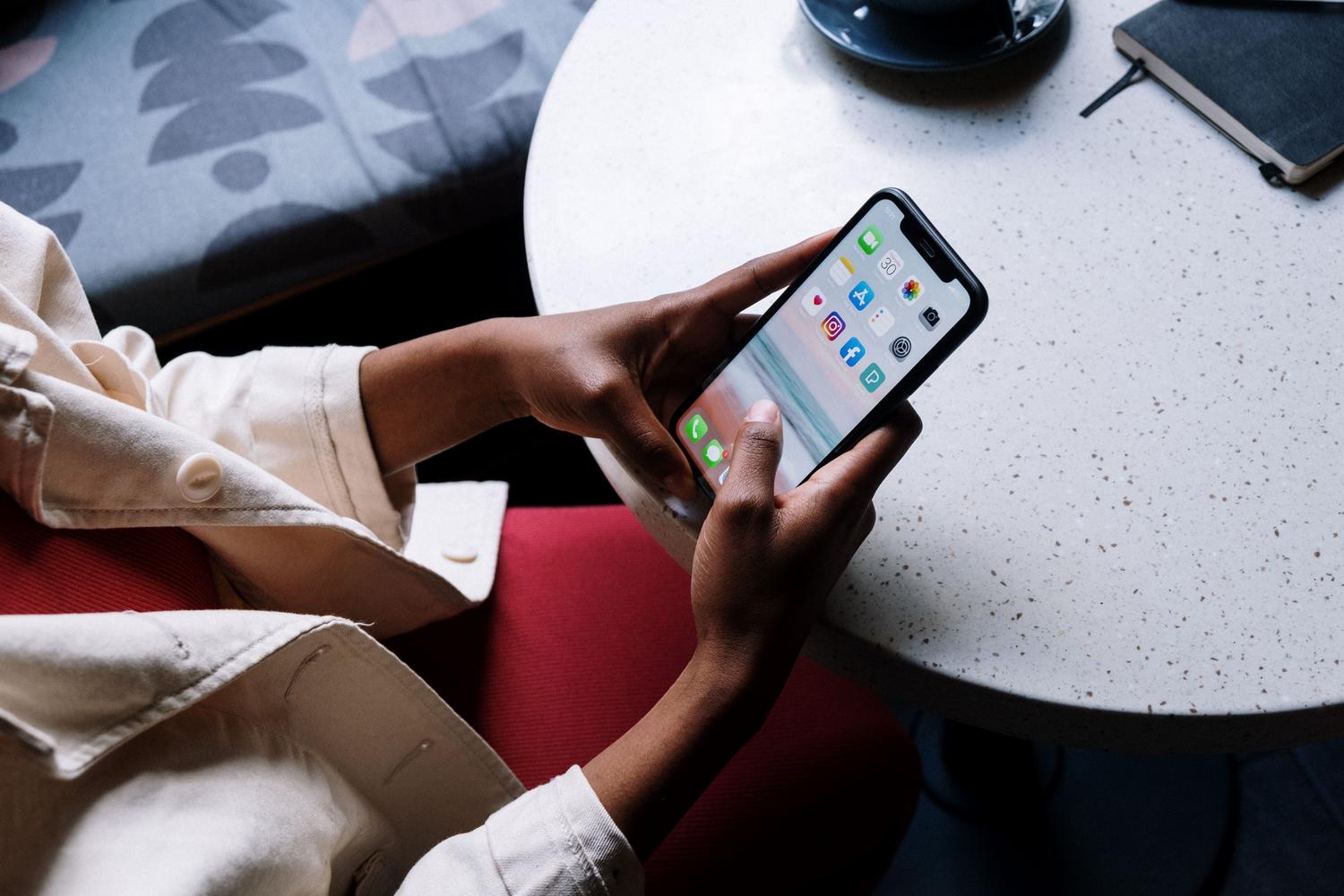 Persona utilizando un teléfono inteligente en una cafetería para gestionar su presencia digital y redes sociales.
