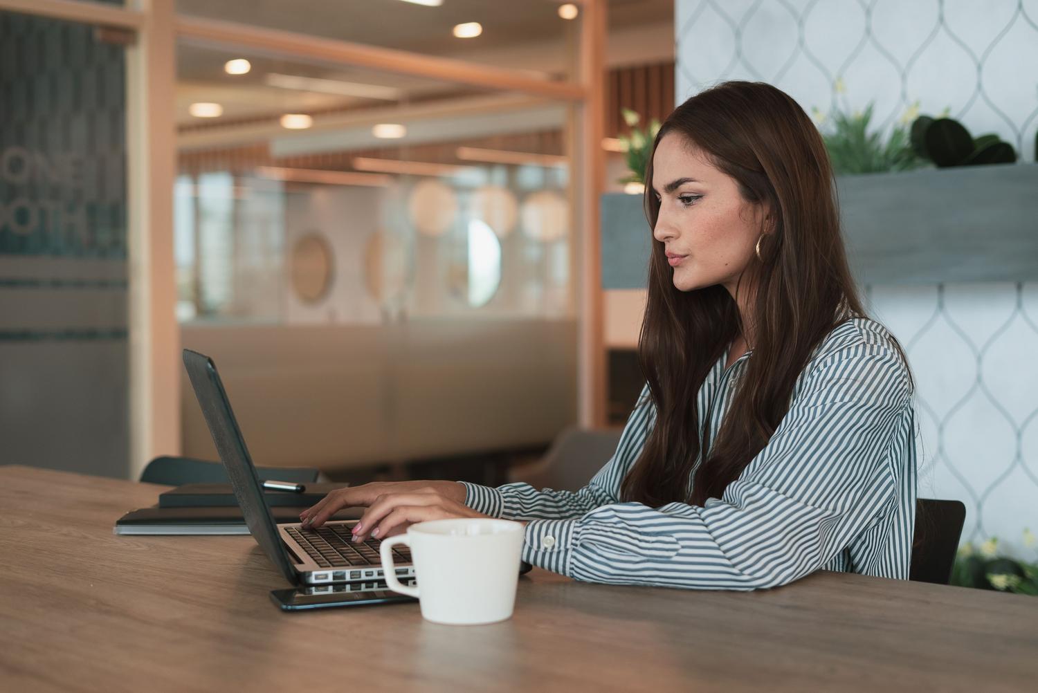 Mujer profesional trabajando con su ordenador portátil en una oficina moderna, representando al usuario gestionando la configuración de su software.