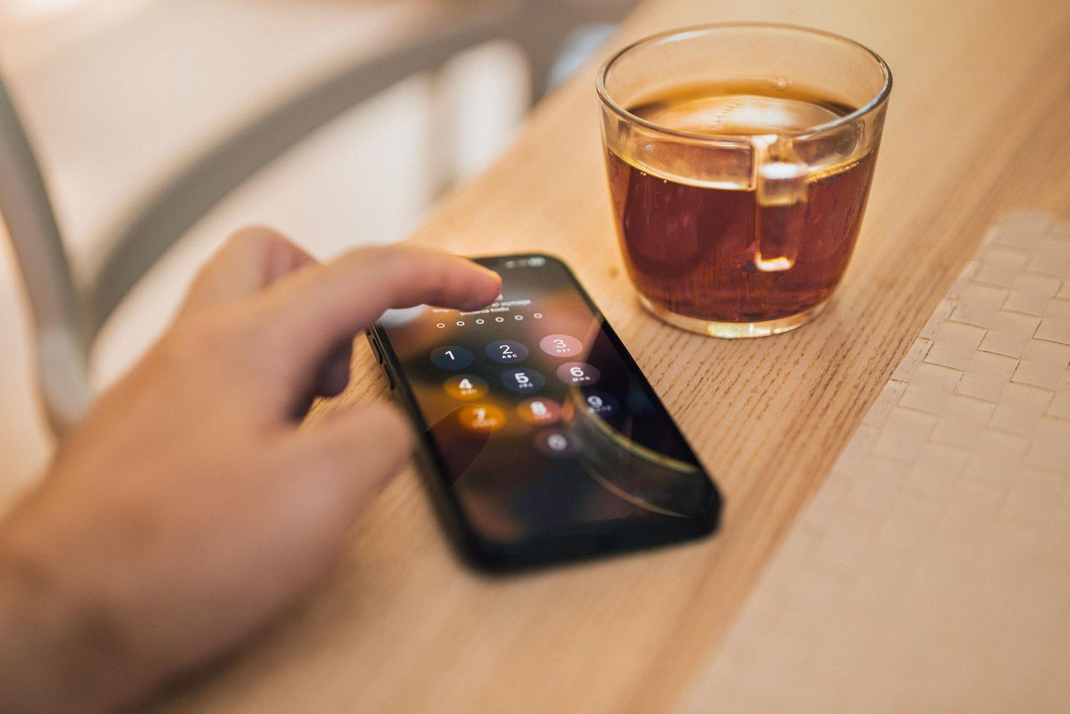 Primer plano de una mano introduciendo un código PIN en la pantalla de un smartphone sobre una mesa de madera.
