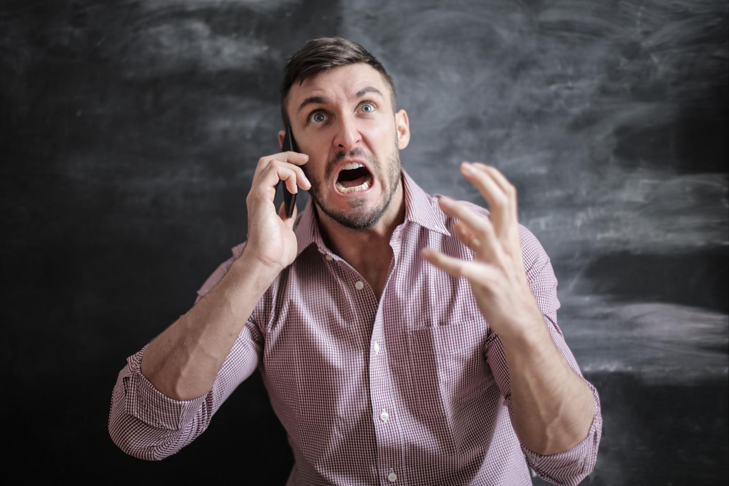 Hombre expresando frustración y estrés mientras utiliza su teléfono móvil, representando la desesperación de no recordar la contraseña.