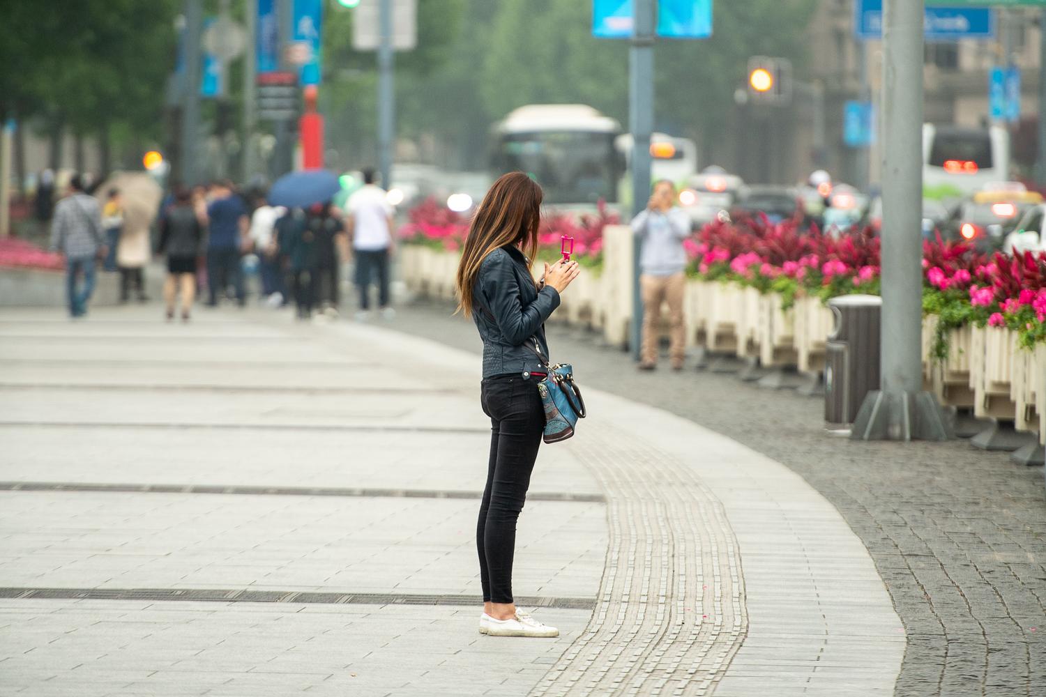 Mujer joven consultando su teléfono móvil en una zona urbana moderna de Shanghái, ilustrando la movilidad digital.