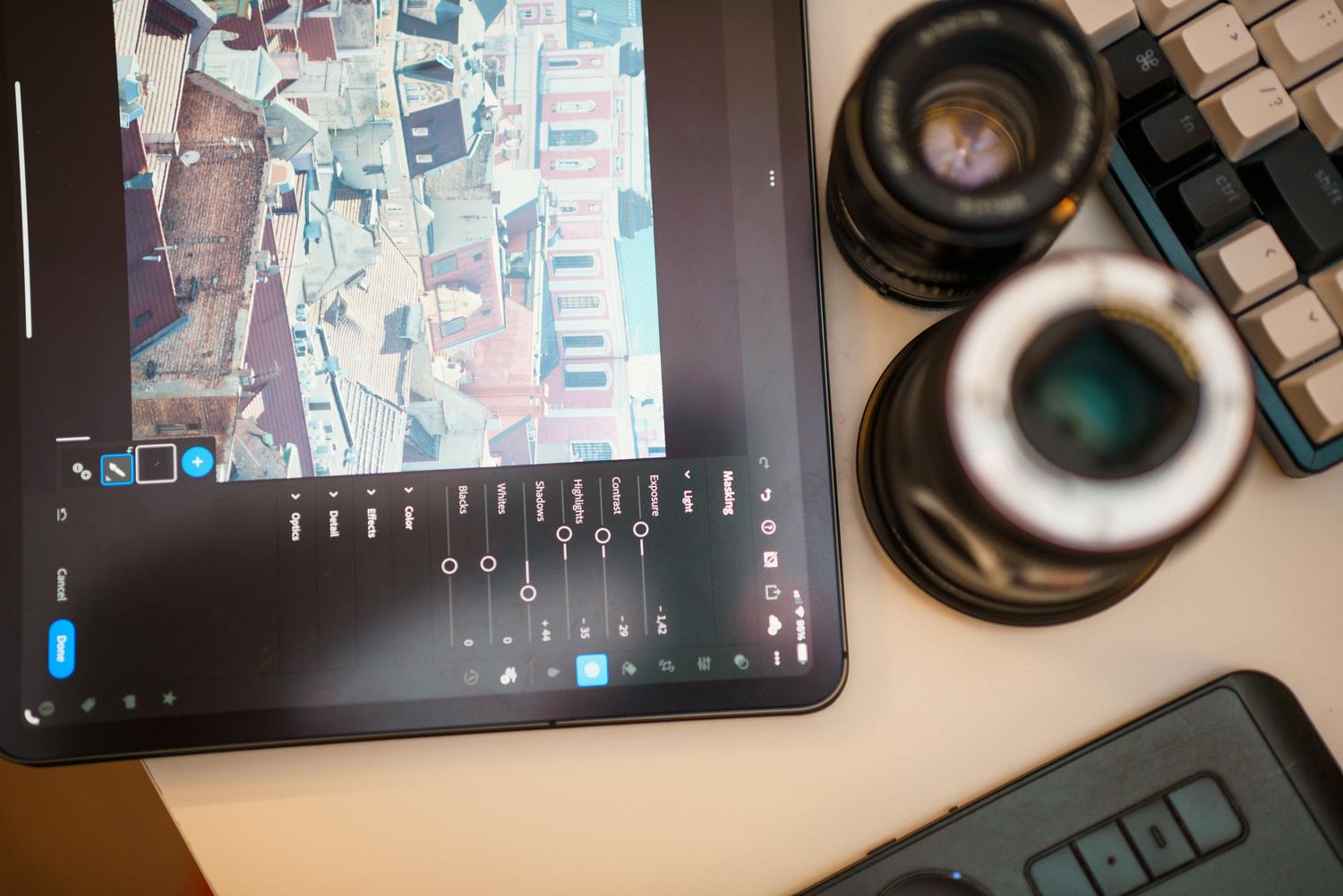 Kit de edición profesional con tableta mostrando una foto de paisaje urbano, lentes de cámara y teclado.