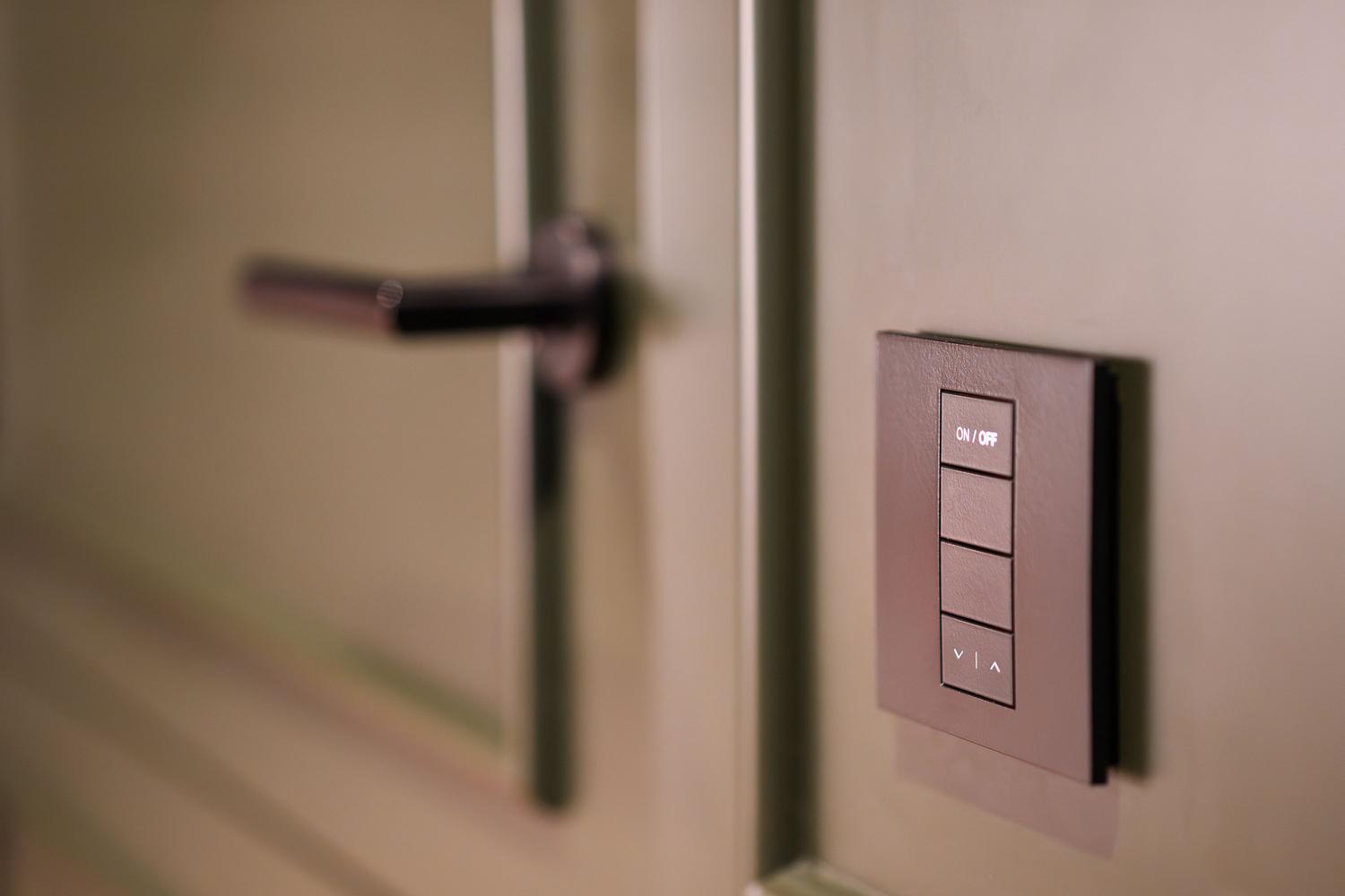 Interruptor inteligente ubicado junto a la puerta de una habitación, manteniendo la comodidad del control físico tradicional.