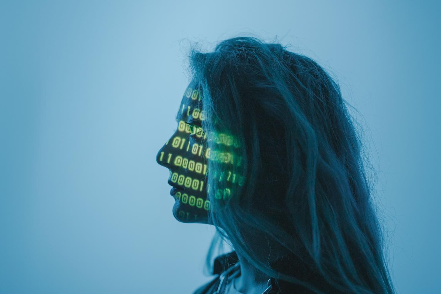 Retrato de una persona con código binario proyectado sobre su rostro, simbolizando el robo de identidad por IA y los deepfakes.