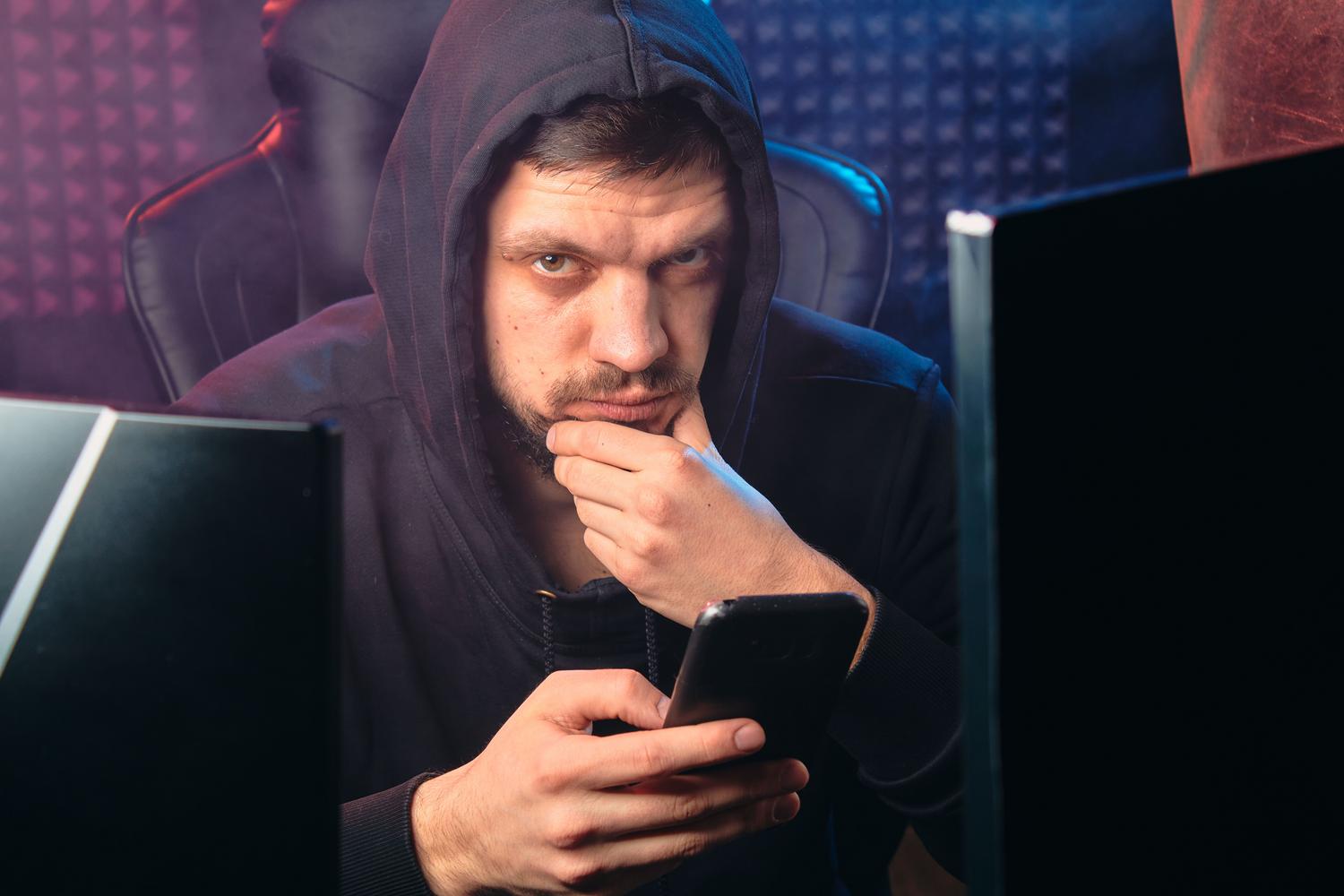 Persona con capucha utilizando un smartphone rodeada de pantallas, representando el phishing hiperpersonalizado y los ataques modernos.