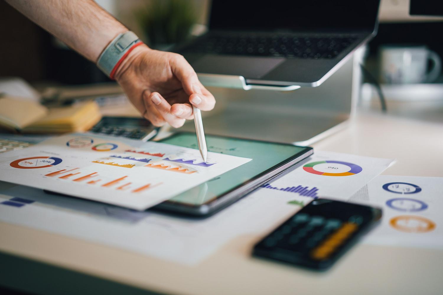 Profesional analizando gráficos financieros y tablas en una tablet y papel, representando el análisis de costes de infraestructura de Kubernetes y la cultura FinOps.