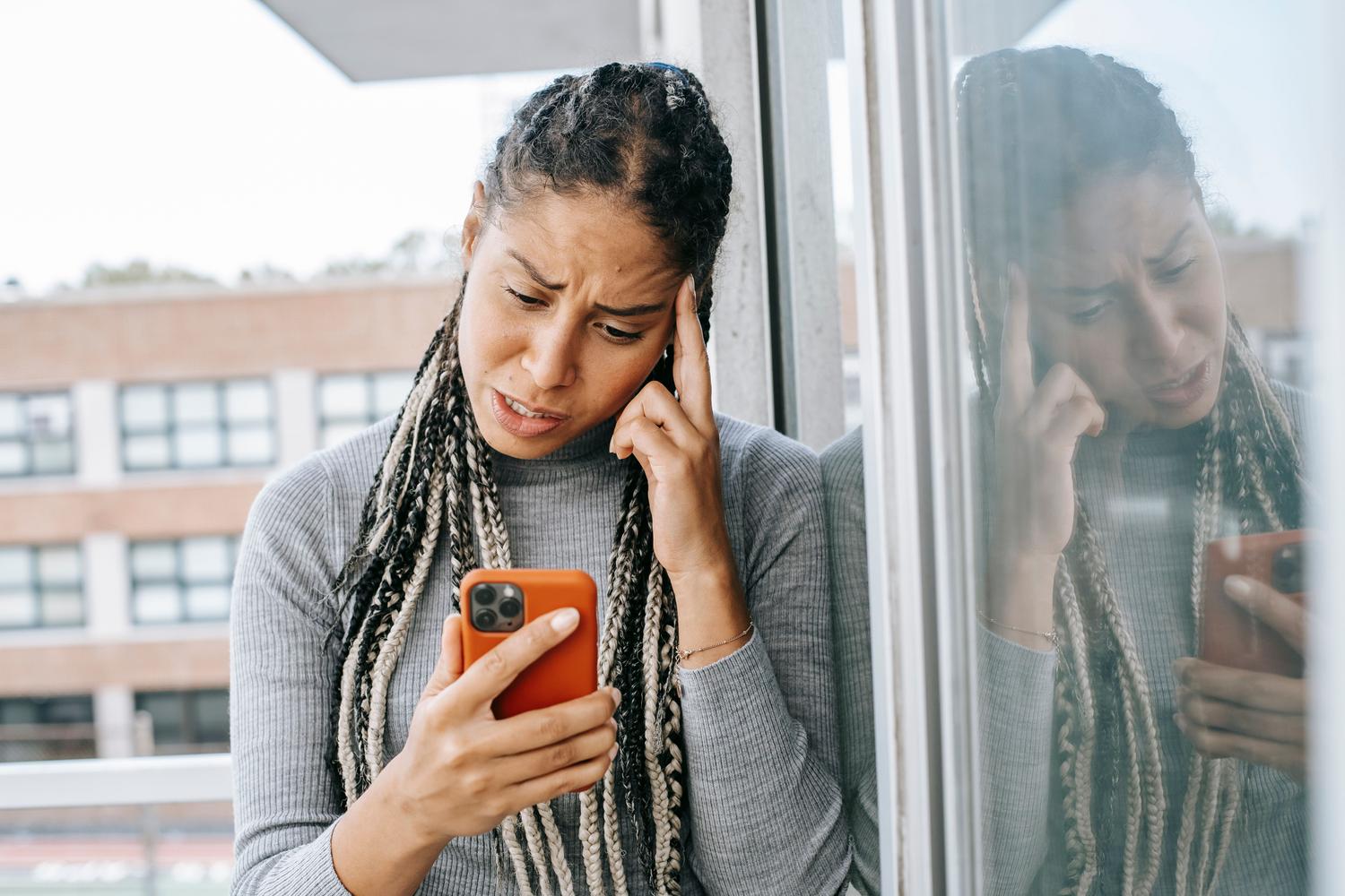 Mujer joven con expresión de decepción mirando la pantalla de su teléfono móvil, representando la frustración por una conexión lenta.