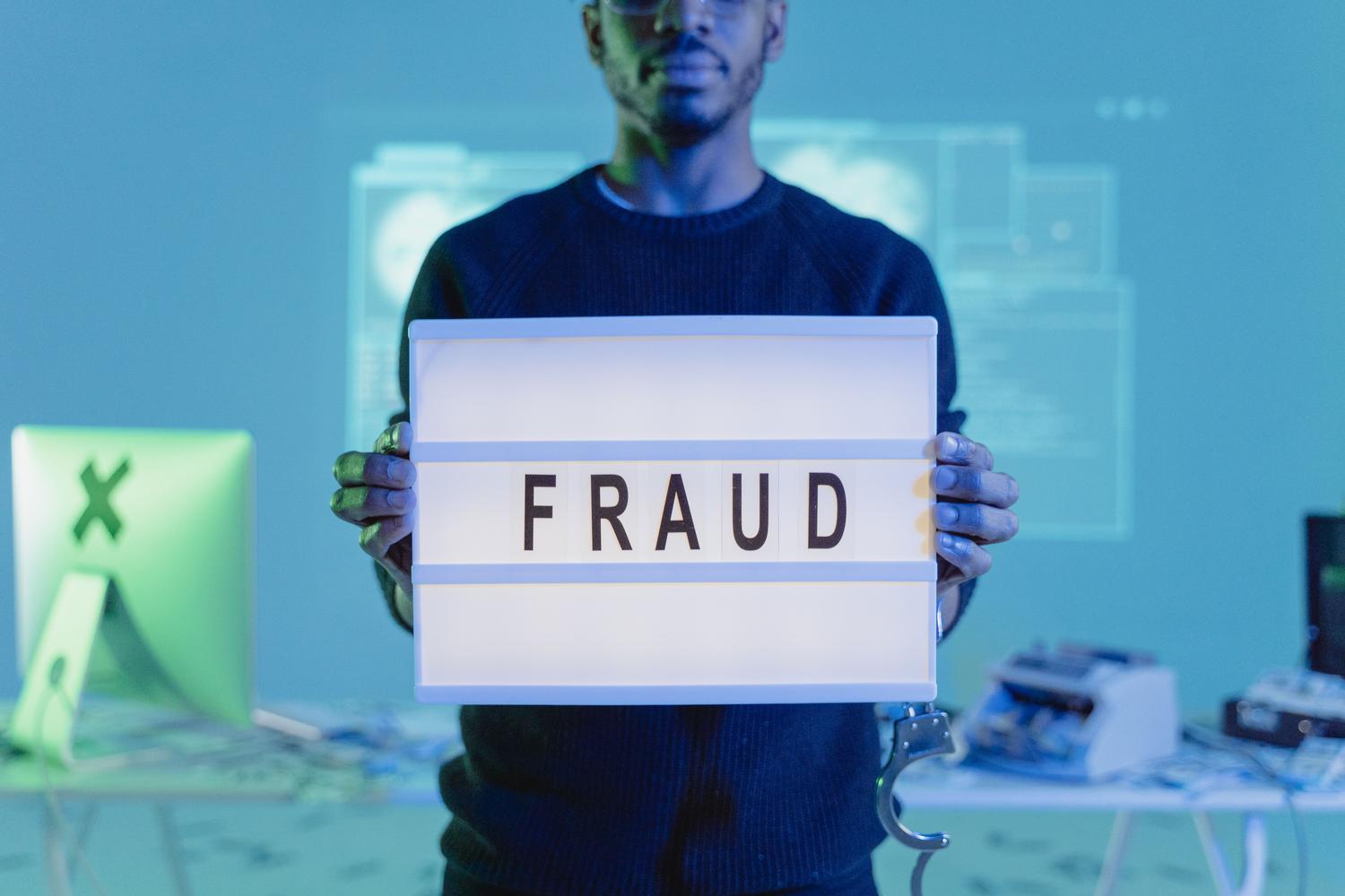 Hombre sosteniendo un letrero que dice FRAUD en una oficina tecnológica, simbolizando la estafa de soporte técnico.