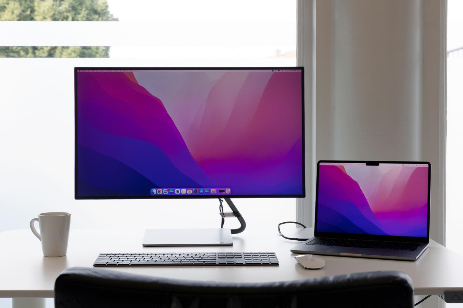 Estación de trabajo moderna y minimalista con un portátil conectado a un monitor externo en un ambiente luminoso.
