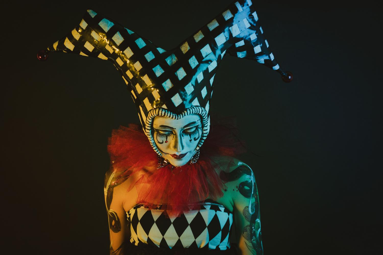 Retrato oscuro y perturbador de un personaje con disfraz de arlequín y maquillaje dramático, representando las mascotas corruptas del juego.