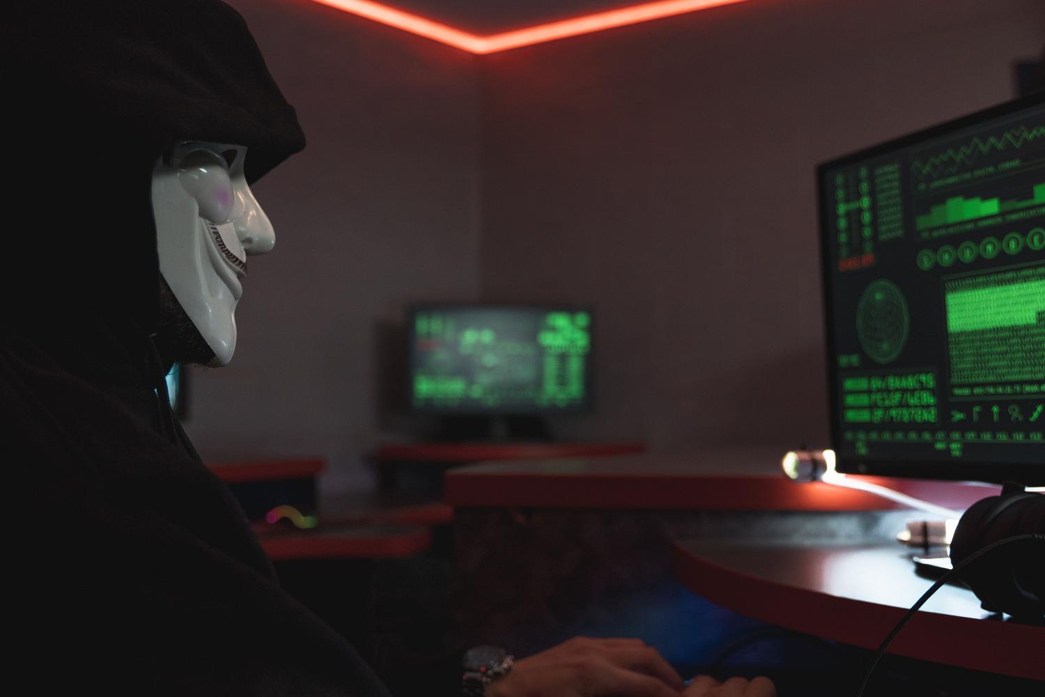Persona con máscara de hacker operando una computadora en un entorno oscuro, ilustrando las amenazas y vulnerabilidades web.