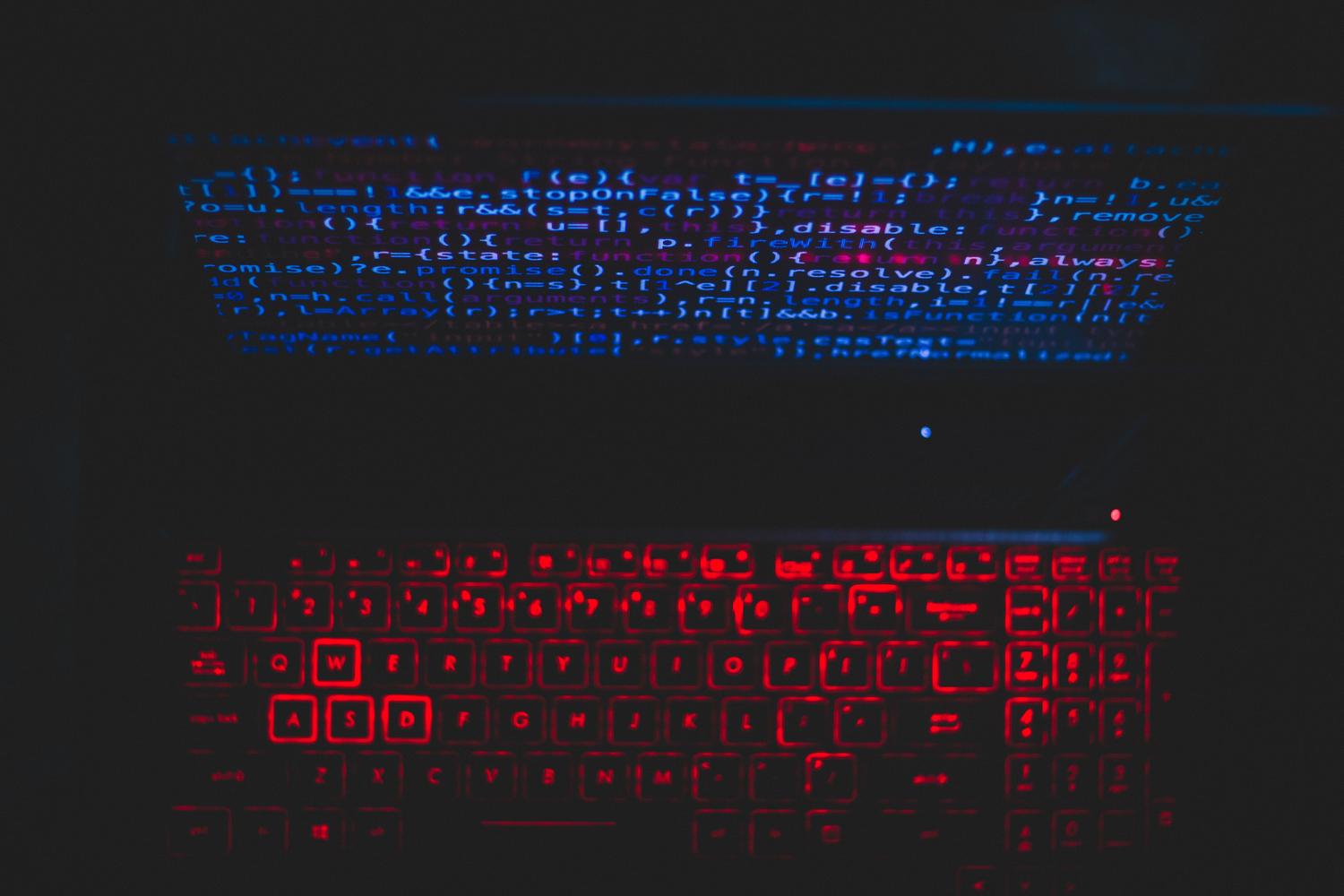 Portátil en un entorno oscuro con teclado iluminado en rojo y código en pantalla, simbolizando los ciberataques y el malware impulsado por IA.