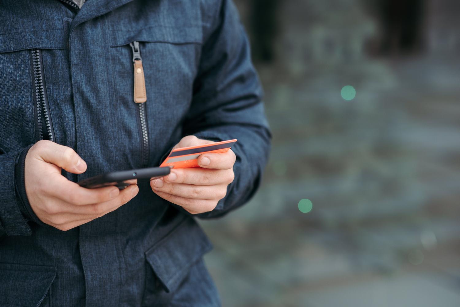 Persona introduciendo datos de tarjeta de crédito en un smartphone en la calle, ejemplificando el riesgo de caer en estafas de phishing.