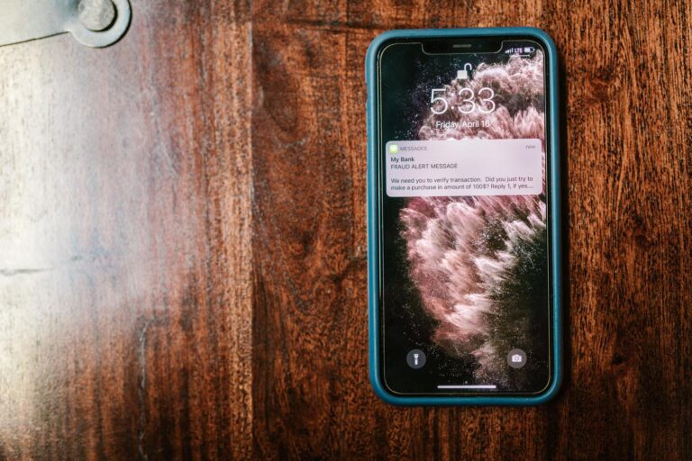 Primer plano de un smartphone mostrando un mensaje de alerta de fraude sobre una mesa de madera, ideal para ilustrar la recepción de alertas de seguridad falsas.