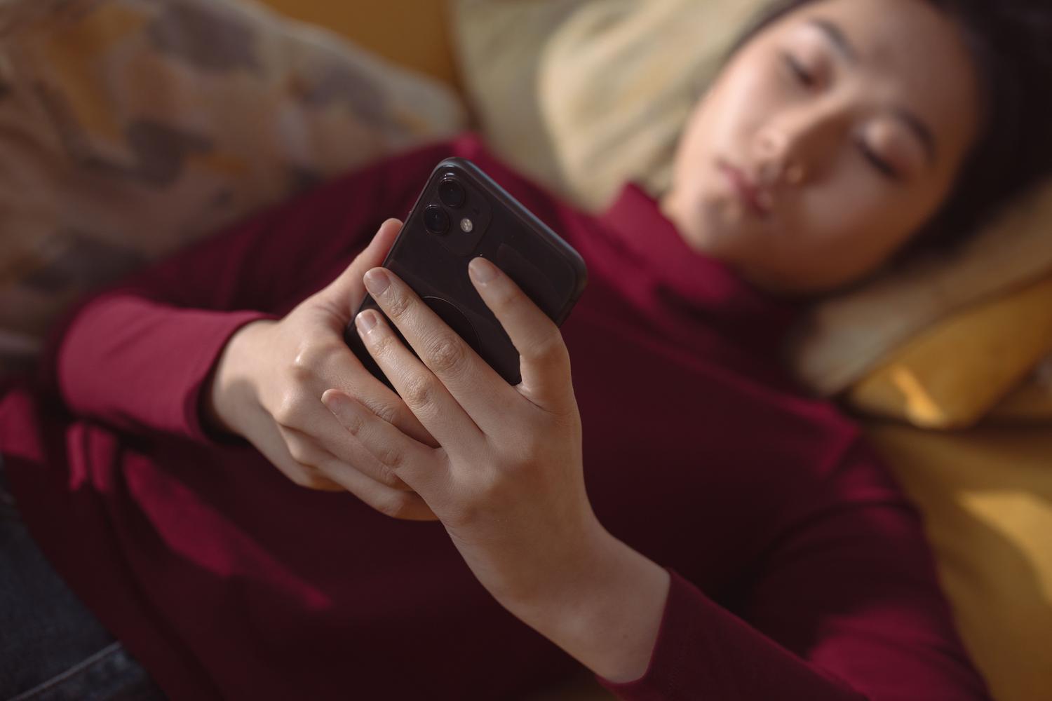 Mujer recostada usando un smartphone para gestionar la configuración de una aplicación de streaming.