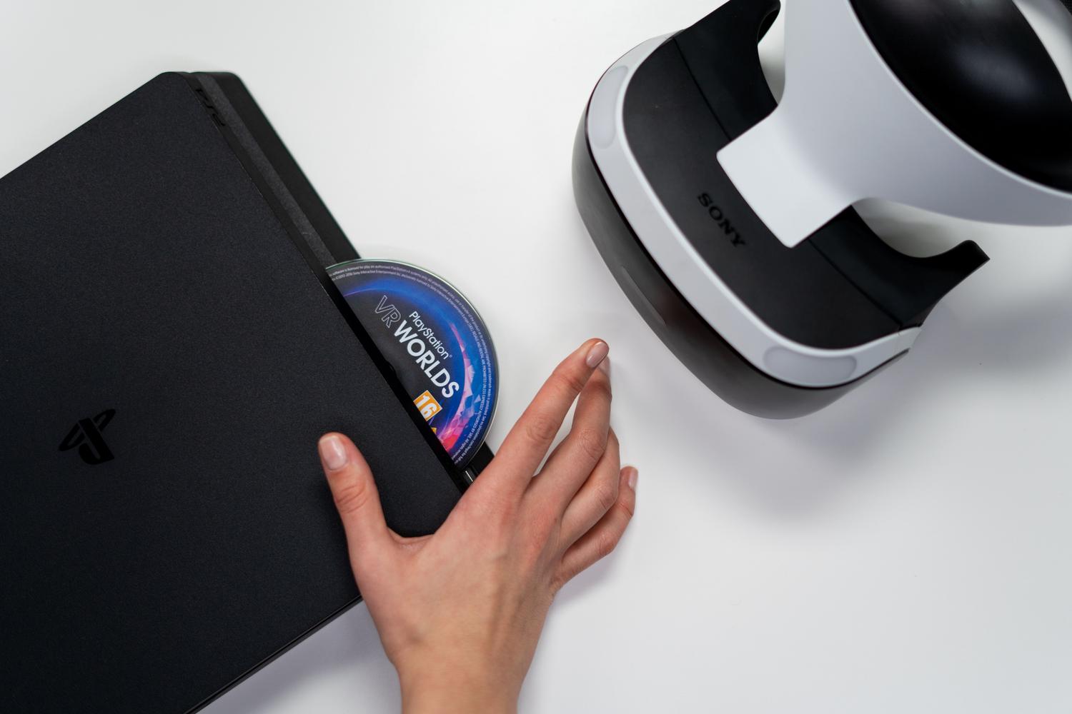 Primer plano de una mano insertando un disco de juego en una consola PlayStation, representando el formato físico tradicional y su interacción tangible.