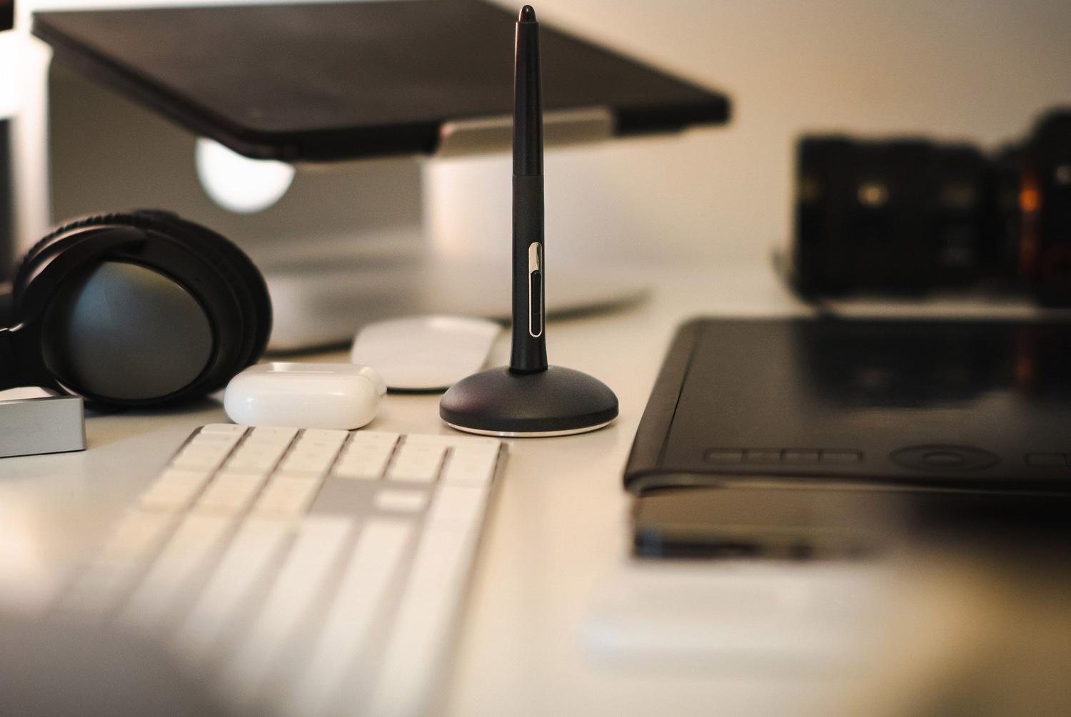 Vista cenital de un espacio de trabajo moderno con tableta gráfica, lápiz digital, teclado y auriculares, ilustrando periféricos de entrada y mixtos.