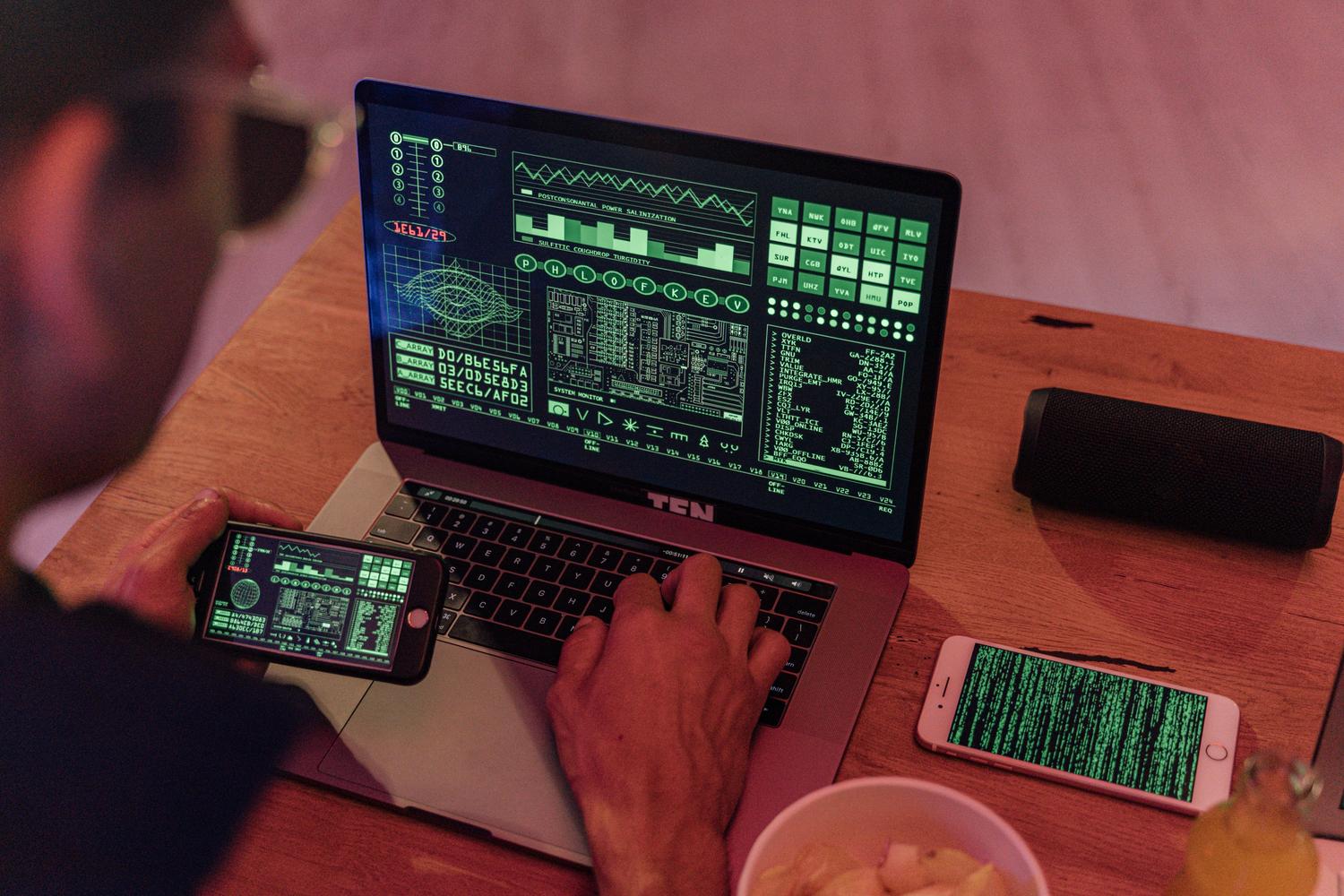 Persona utilizando simultáneamente un portátil y un teléfono móvil con interfaces tecnológicas, representando la autenticación de doble factor (MFA).