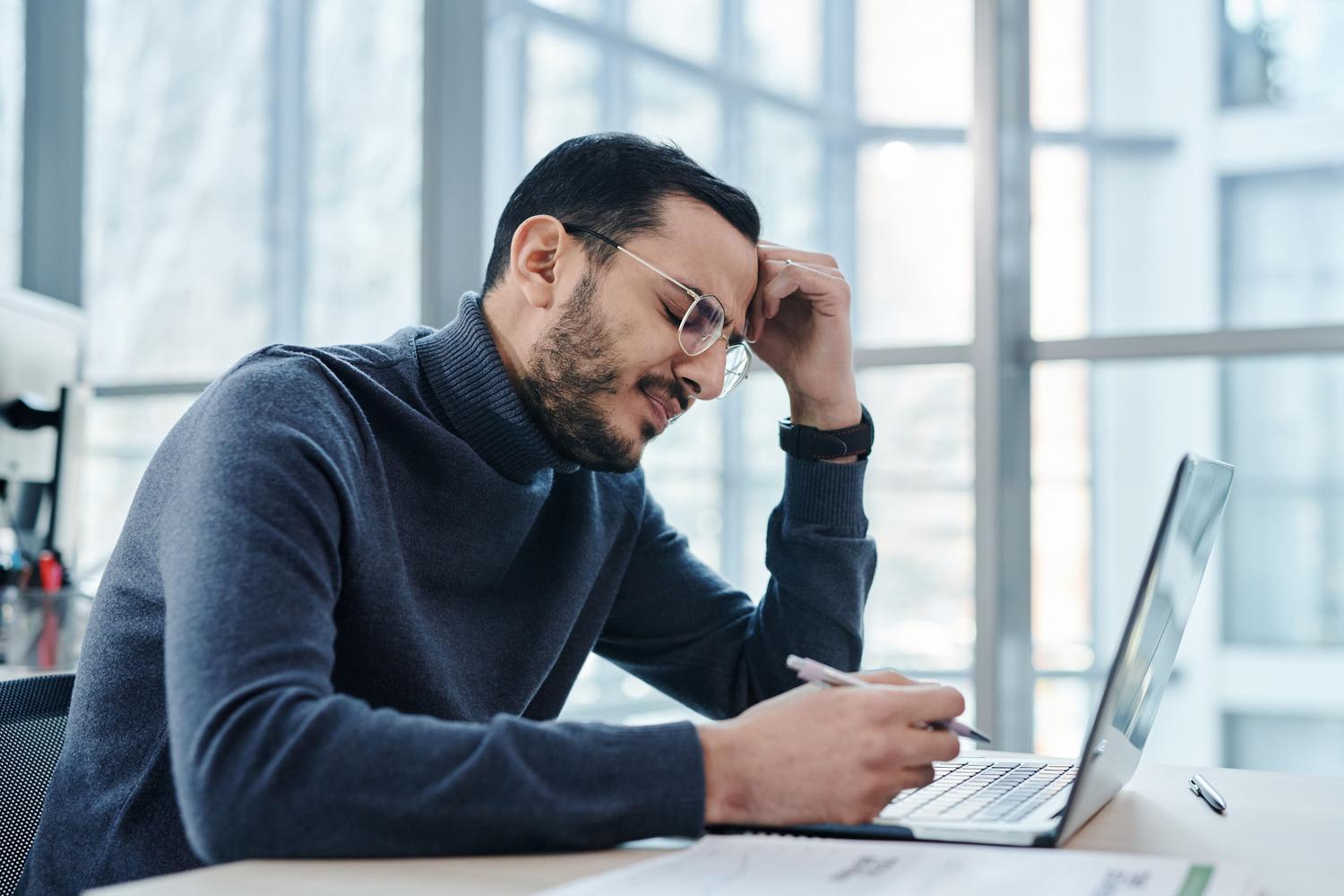 Hombre estresado en oficina moderna intentando solucionar un problema técnico en su portátil